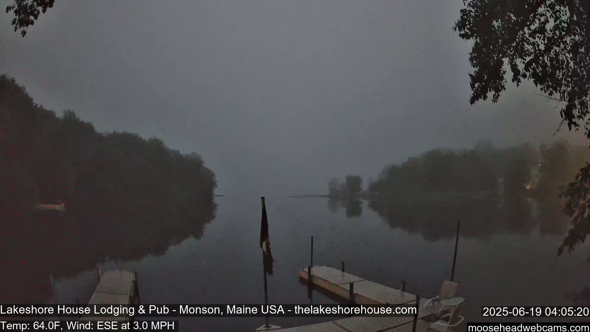 A foggy, calm lake is seen from a dock, with dark trees lining the shore.