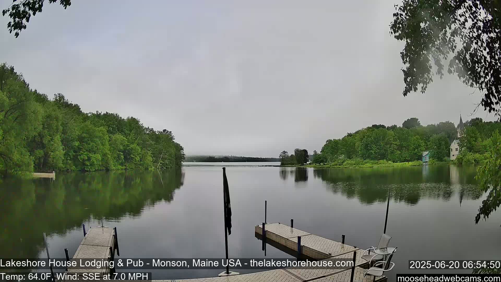 A calm lake, under an overcast sky, is bordered by lush green trees and features two wooden docks.