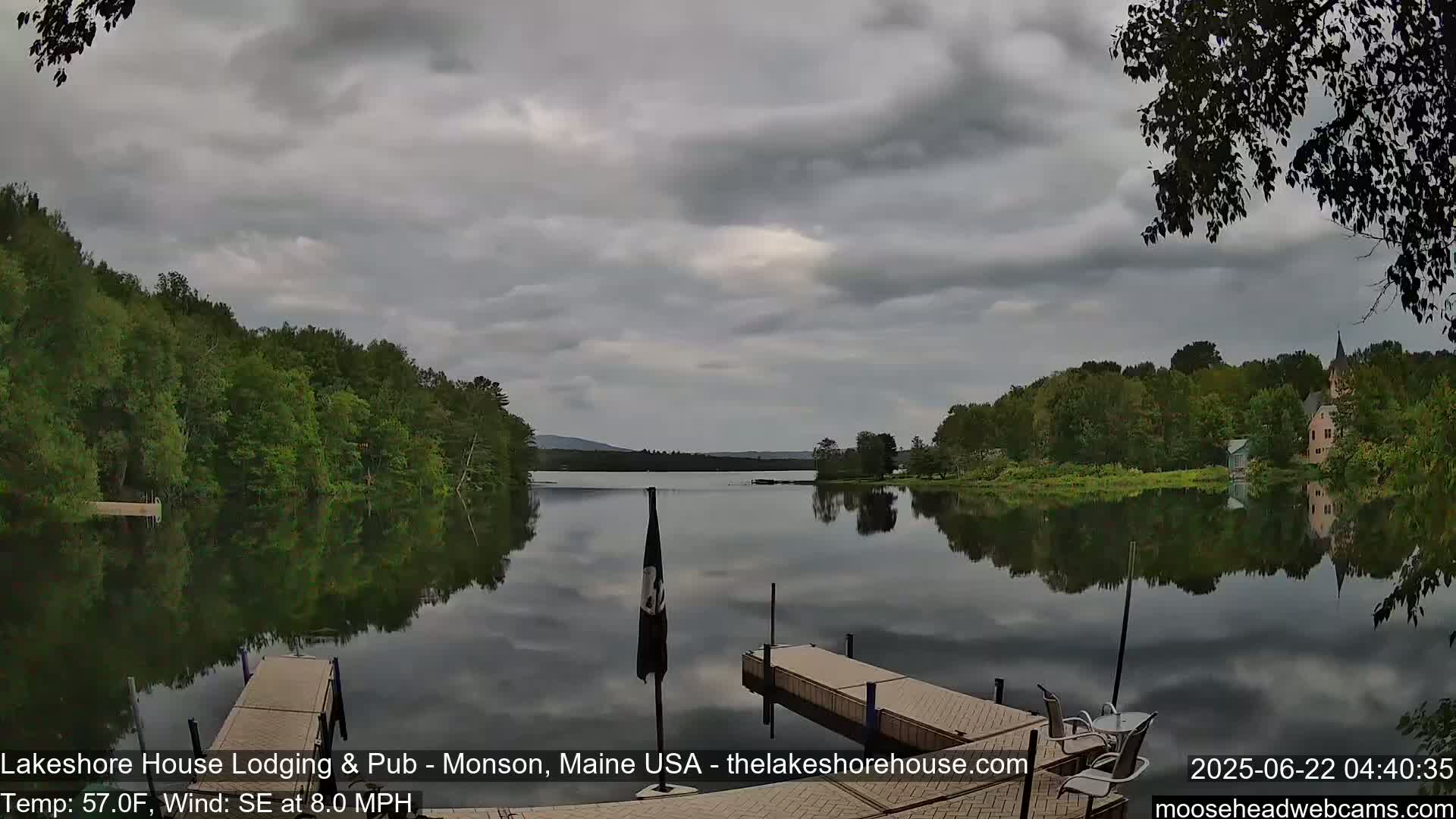 A calm lake reflects overcast skies and tree-lined shores, with two wooden docks extending into the water under a southeastern wind of 8 mph.