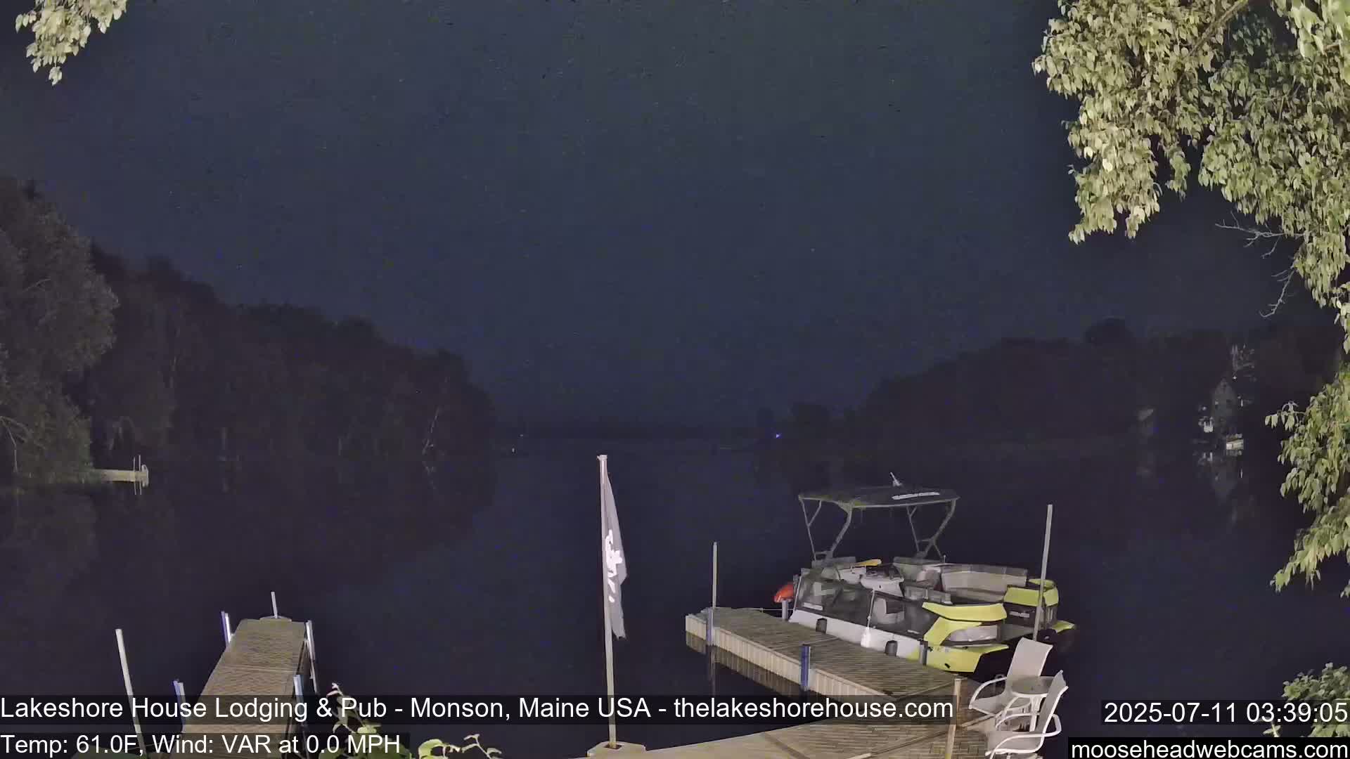 A nighttime view of a calm lake with a pontoon boat docked on a pier under a dark, clear sky.