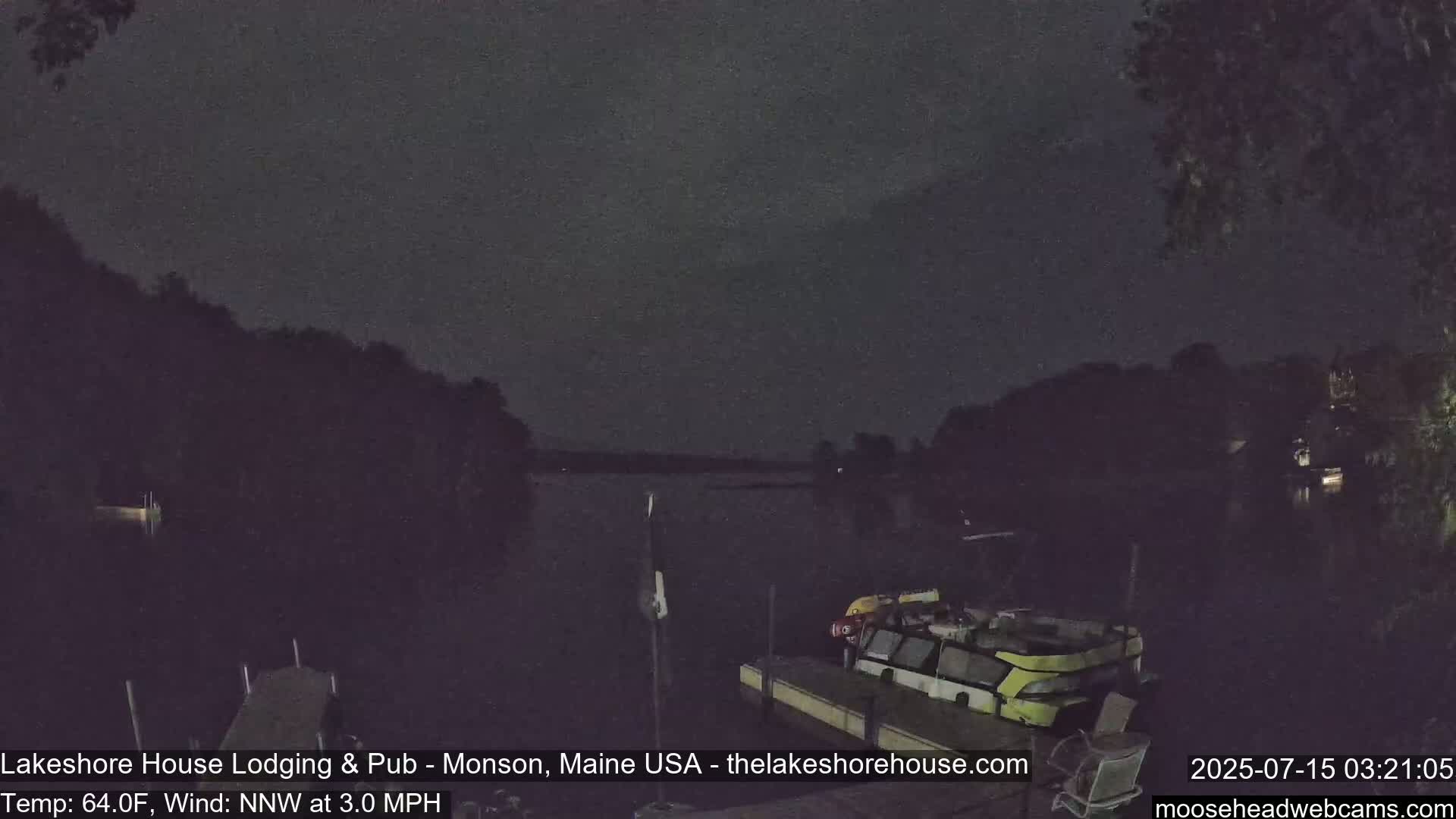 A nighttime view of a calm lake with boats docked at a pier, under a dark sky with a slight wind.