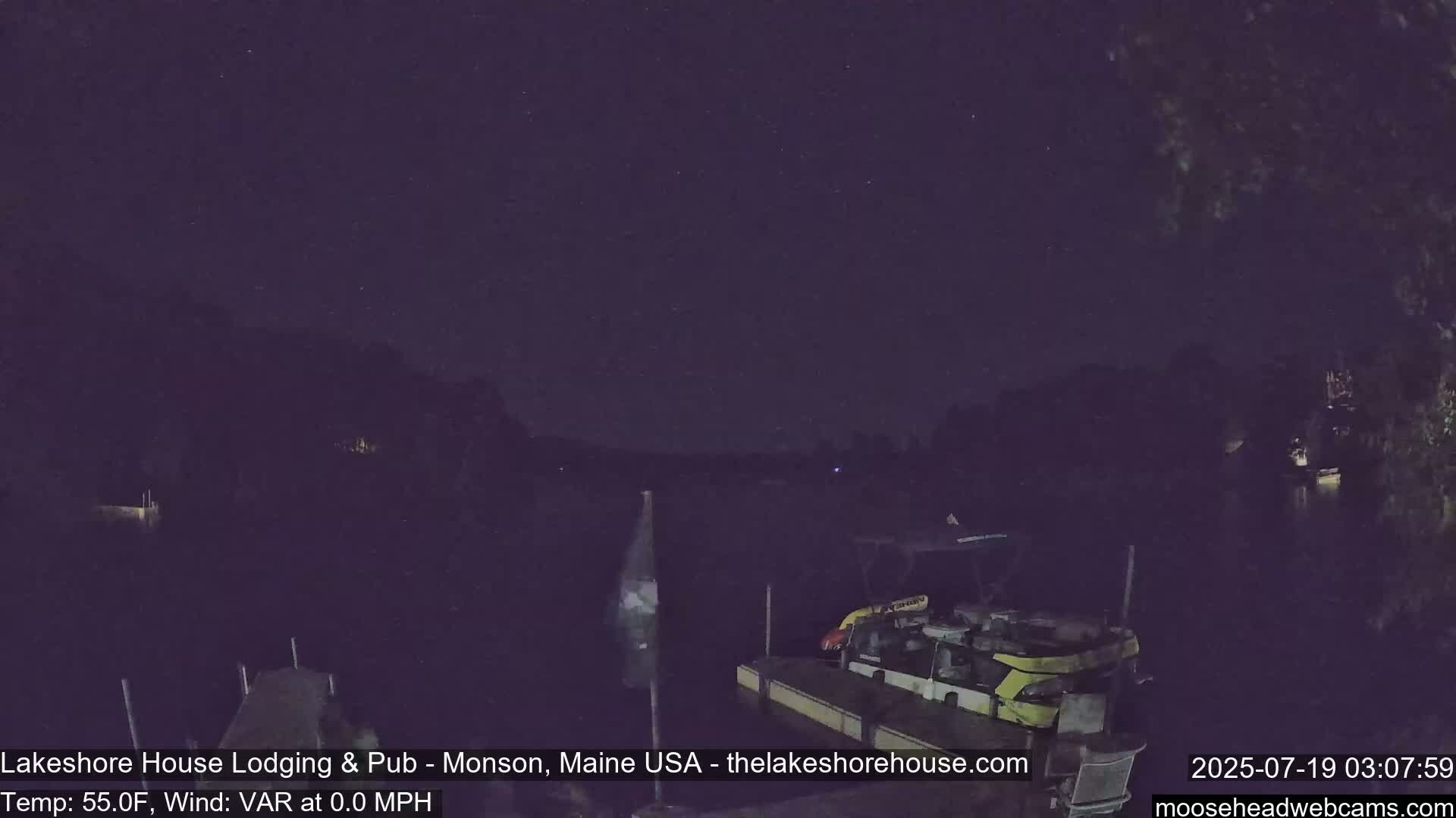 A nighttime view of a dark body of water with a dock and boat, under a clear, starry sky.