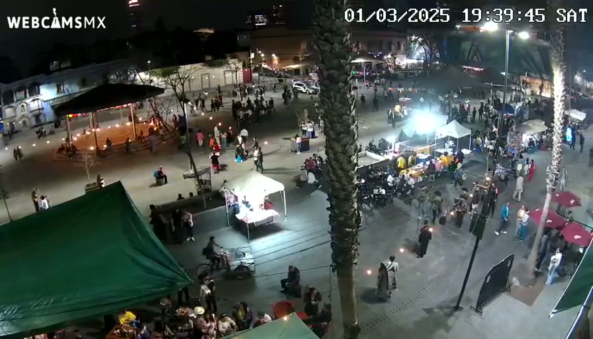 A nighttime aerial view of a crowded plaza with numerous food stalls and people gathered under ambient lighting.