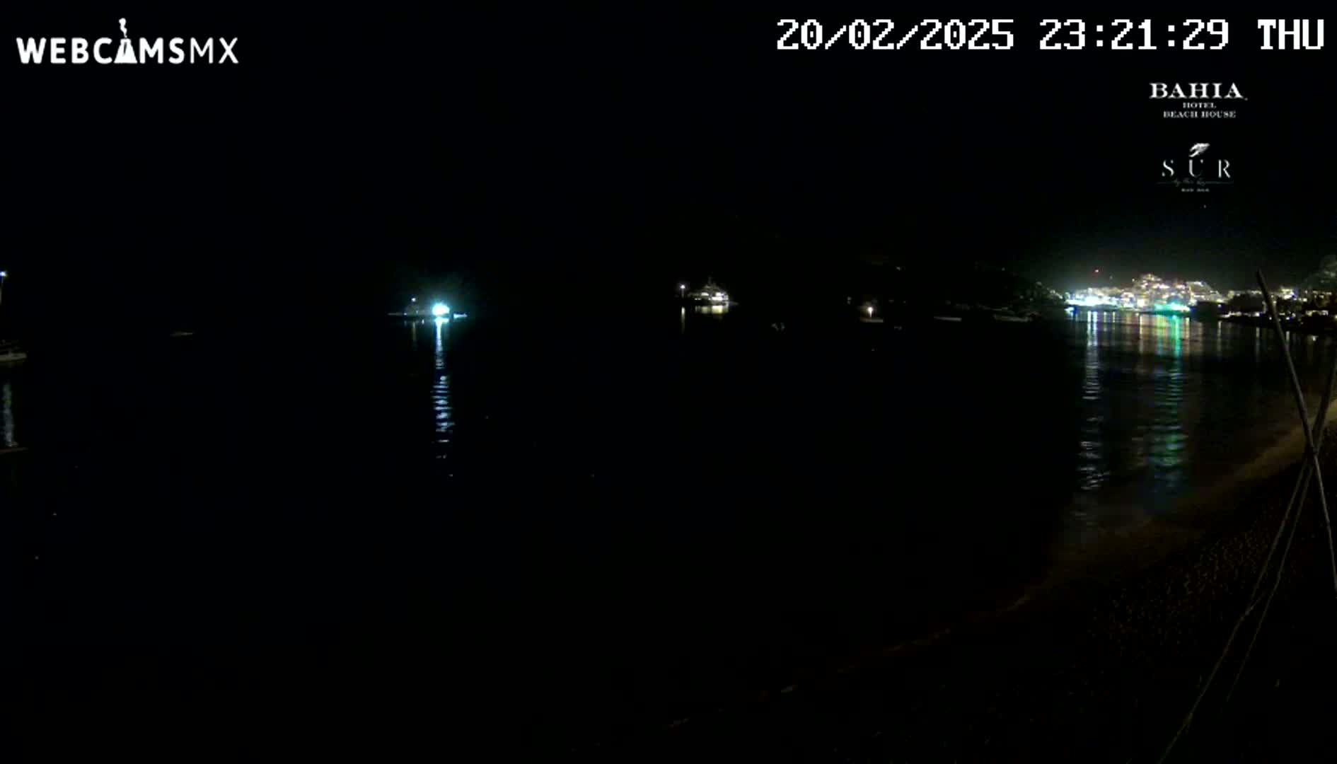 A nighttime view of a dark body of water reflecting city lights across the bay under a clear sky.