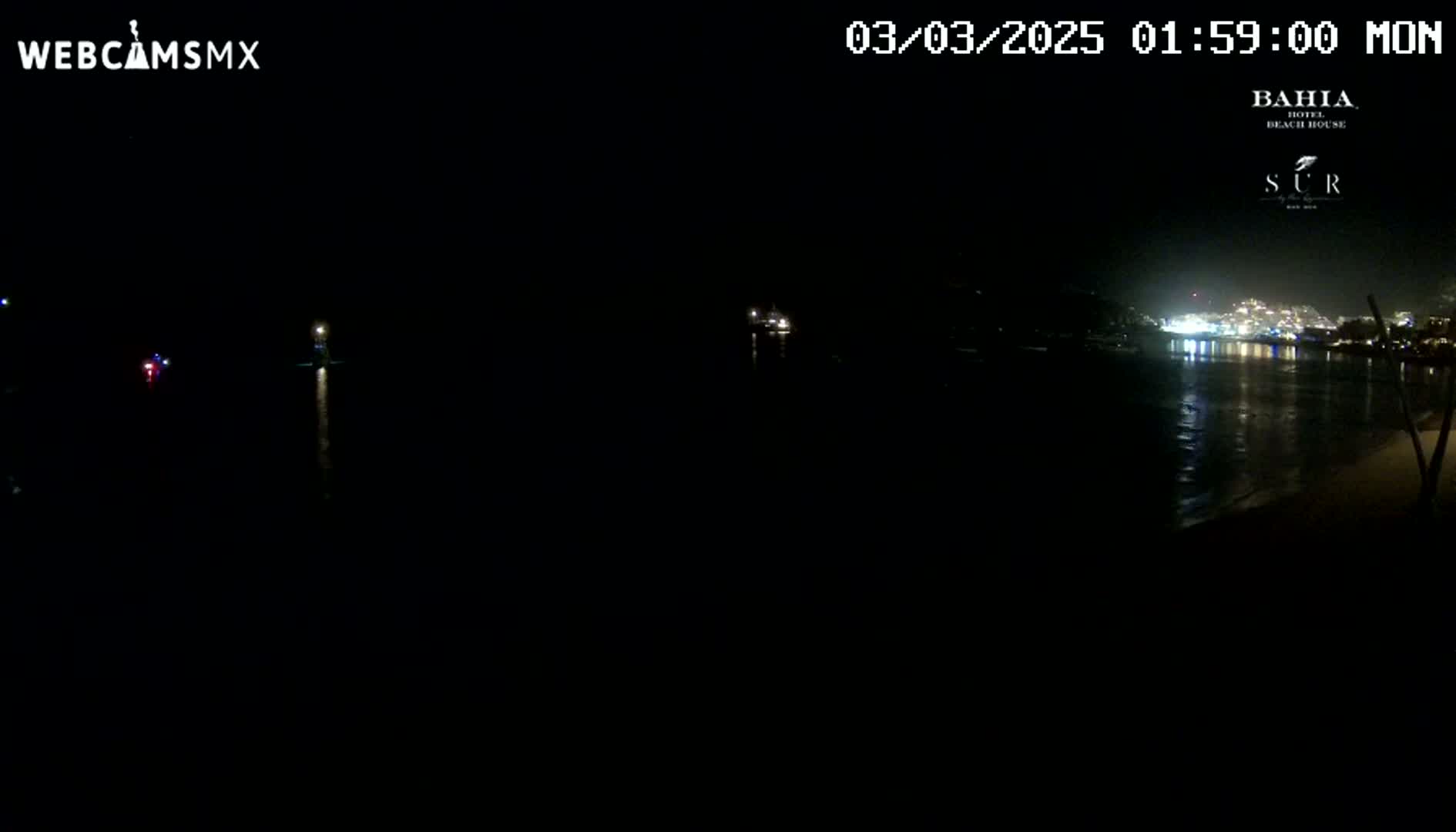A dark nighttime view of a calm body of water reflecting the lights of a distant town.