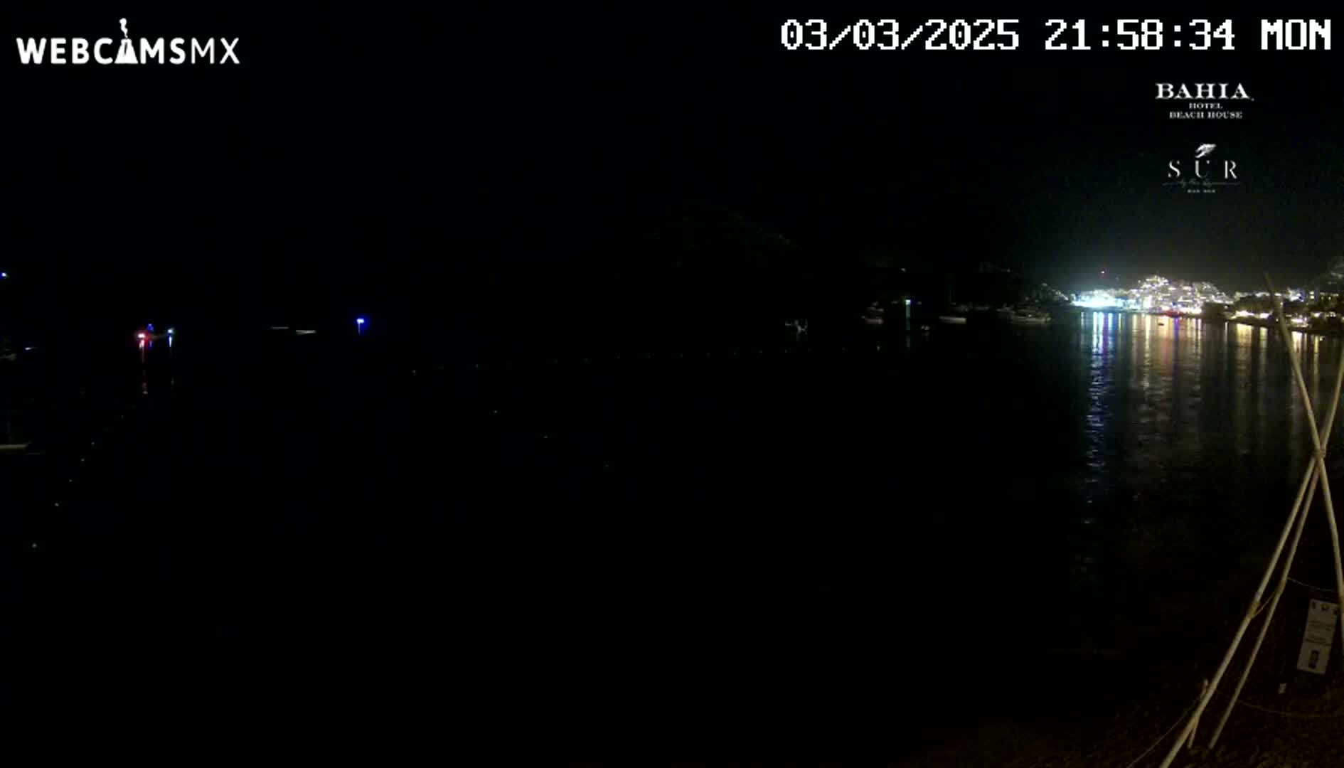 A nighttime view of a dark body of water reflecting the lights of a town across the water, under a clear, dark sky.