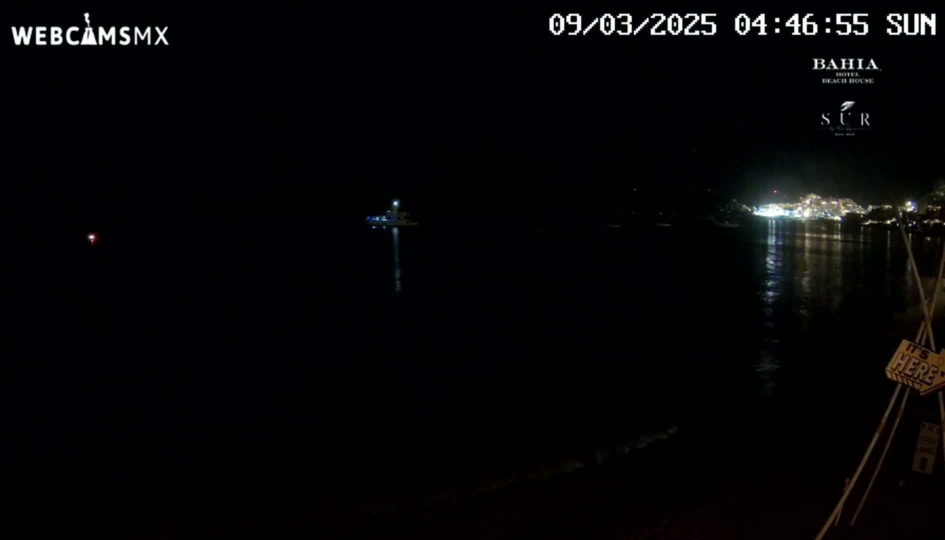 A nighttime, dark view of a calm body of water with a small boat and a distant, illuminated shoreline.