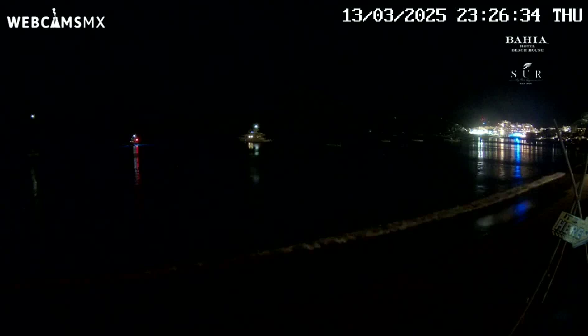 A nighttime view of a dark body of water with a few lights visible on boats and across the far shore.