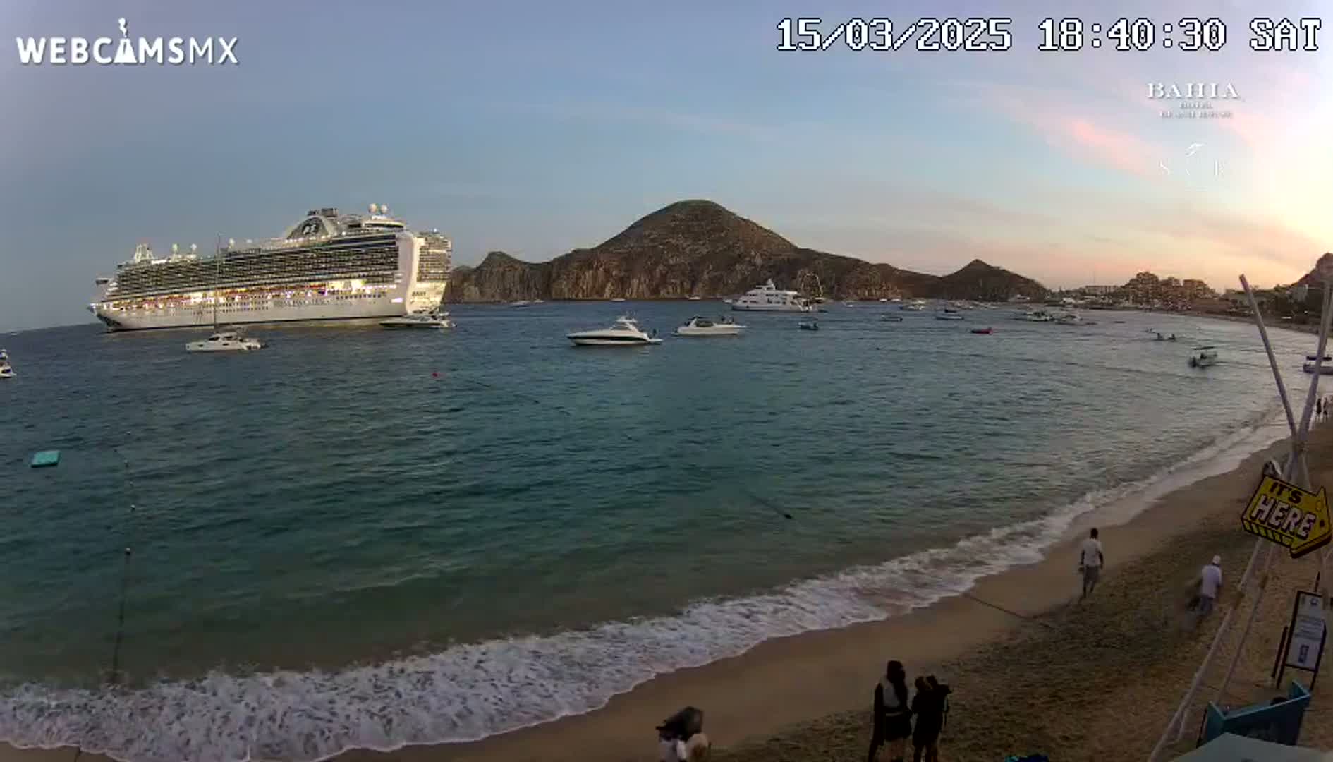 A large cruise ship is anchored offshore near a beach with calm waves under a twilight sky.
