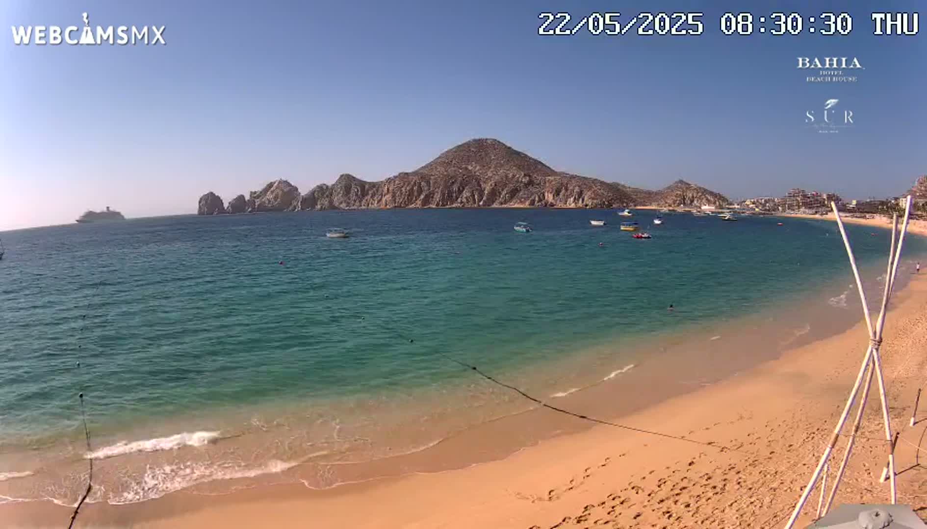 A sandy beach with calm, turquoise water and a mountainous peninsula in the background under sunny skies.