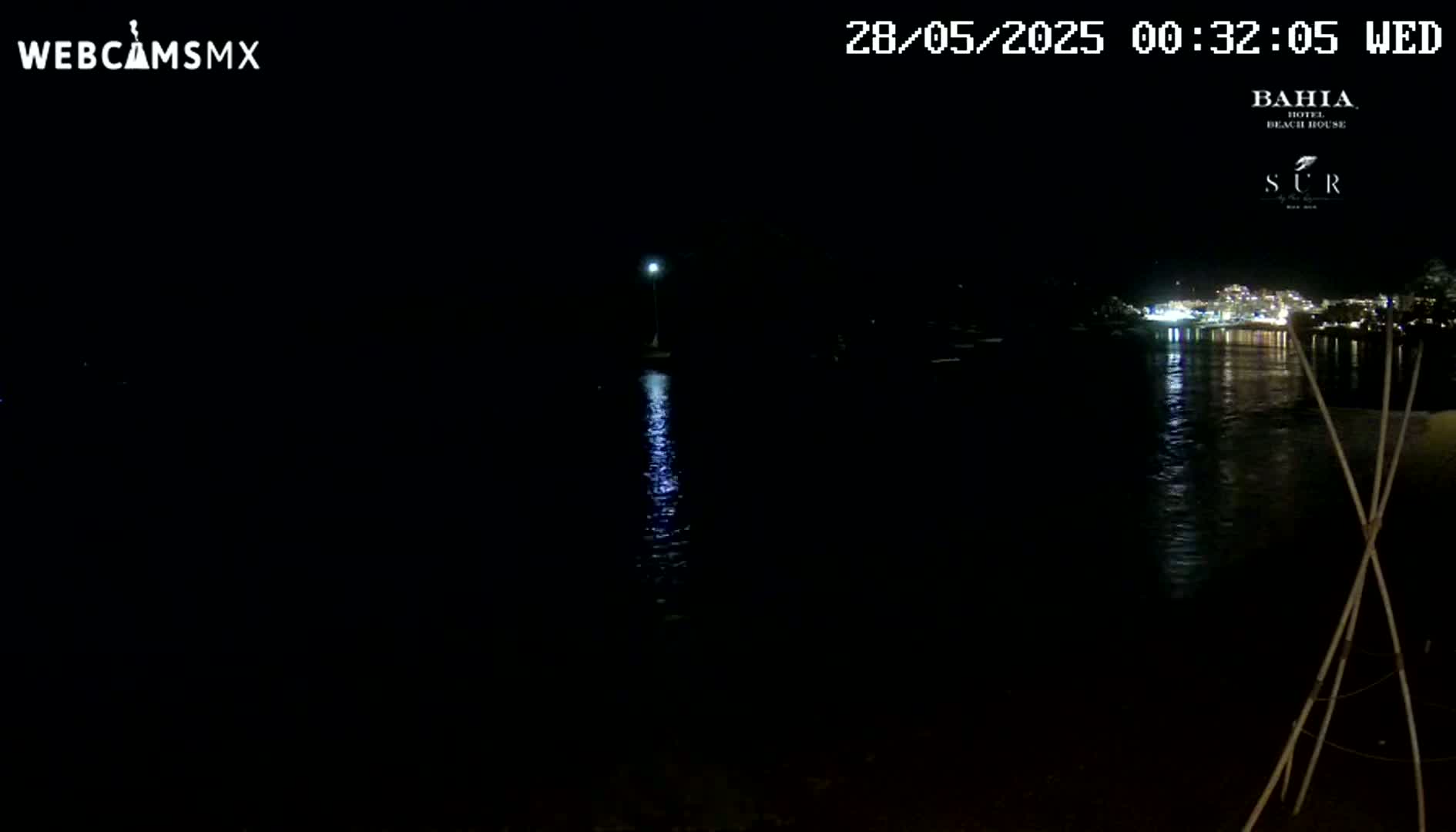 A nighttime view of a calm body of water reflecting lights from a distant shoreline under a clear, dark sky.