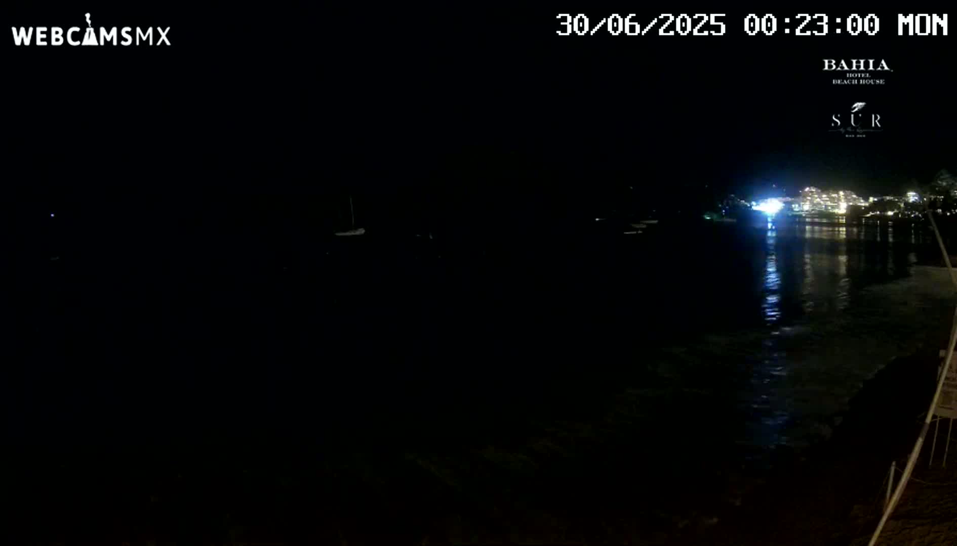 A nighttime view of a dark body of water reflecting the lights of a distant building, under a clear sky.