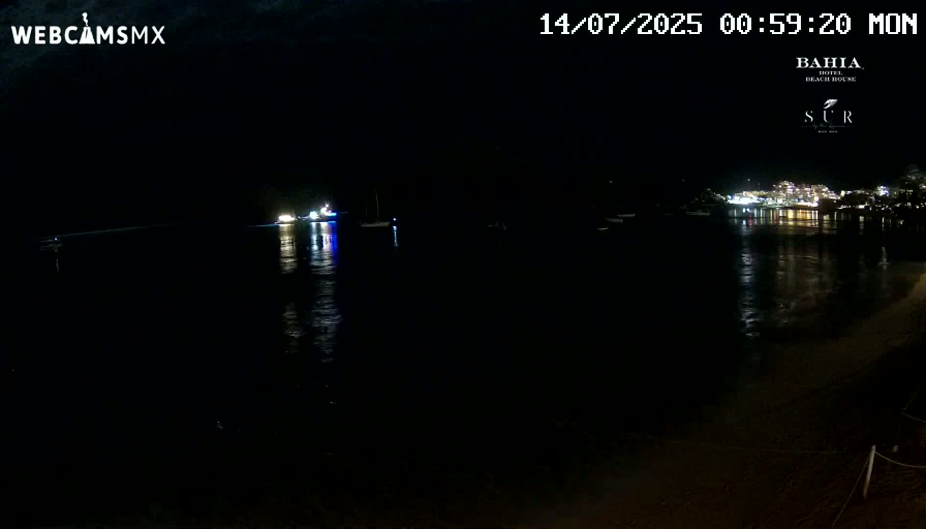 A dark nighttime view of a calm body of water with faintly lit boats and a distant illuminated shoreline.