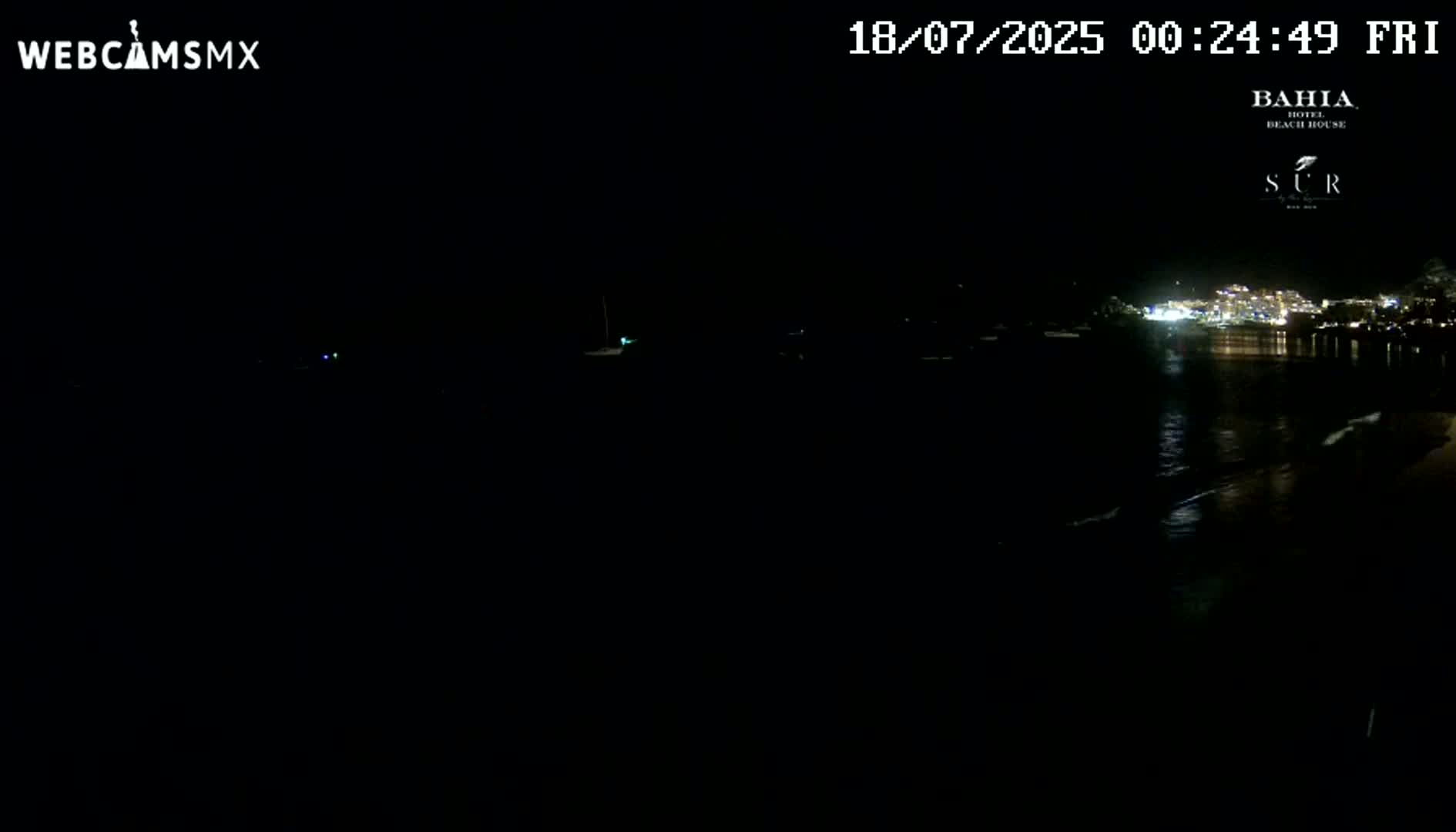 A nighttime view of a dark body of water with faintly visible lights from a distant town across the water under a clear, dark sky.