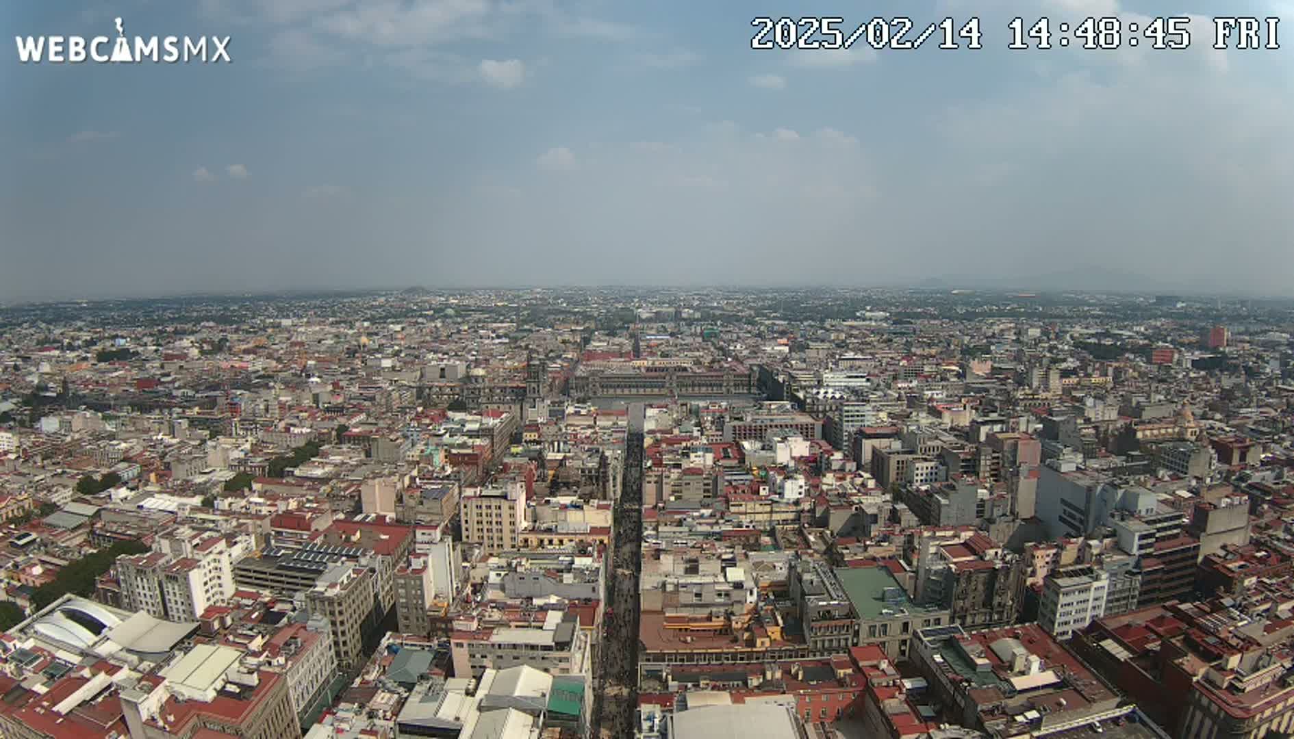 A high-angle, long shot on a partly cloudy day shows a sprawling cityscape extending to the horizon.