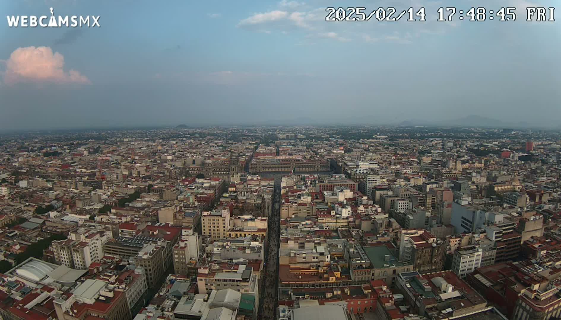 A hazy, high-angle view of a vast cityscape, possibly at dusk, shows a dense collection of buildings extending to the horizon.