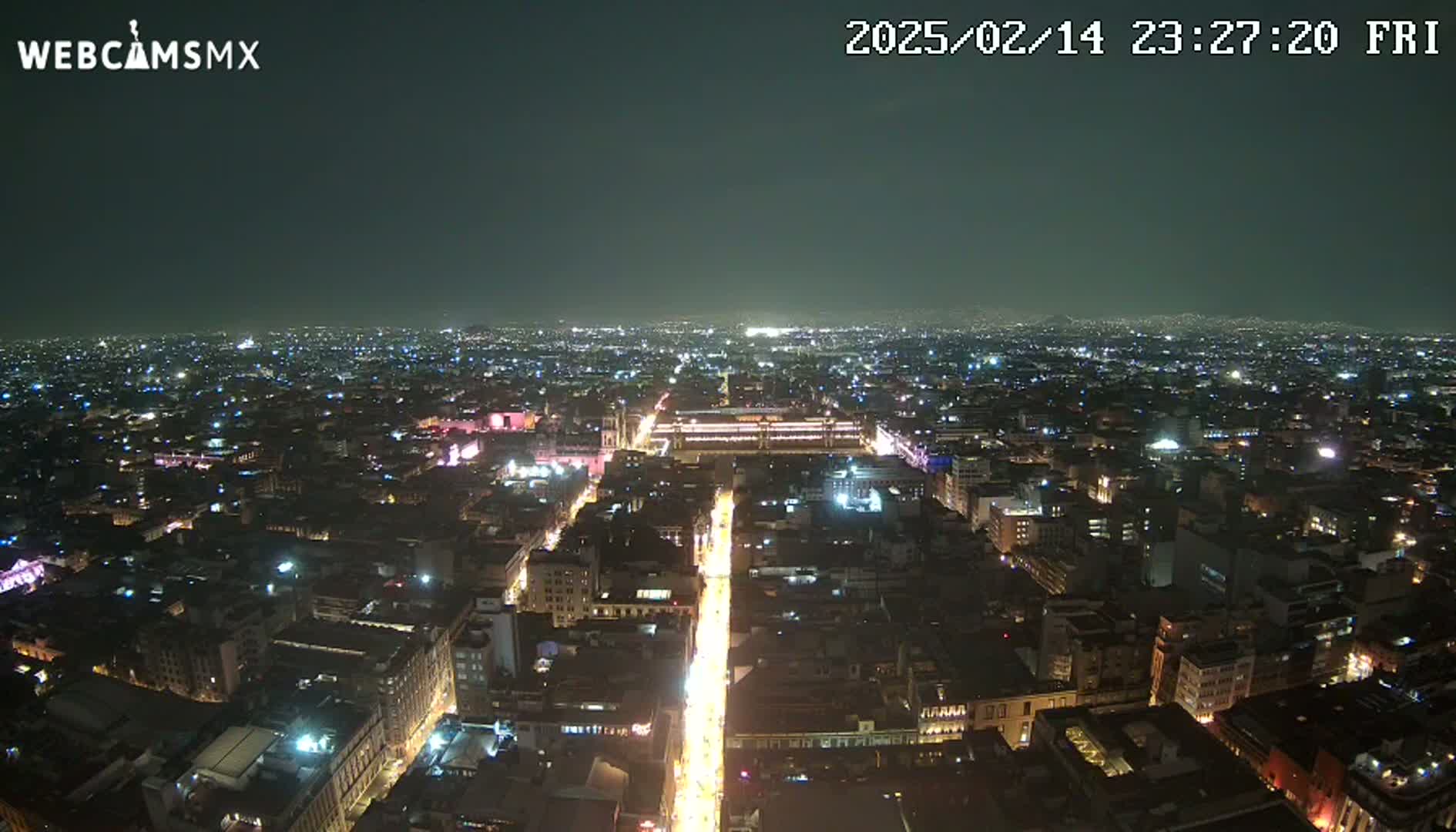 A nighttime aerial view of a sprawling city with illuminated streets and buildings under a clear, dark sky.