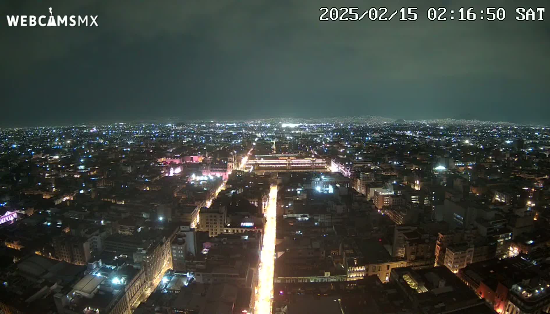 A nighttime, high-angle view of a city illuminated by streetlights and building lights under a dark, overcast sky.