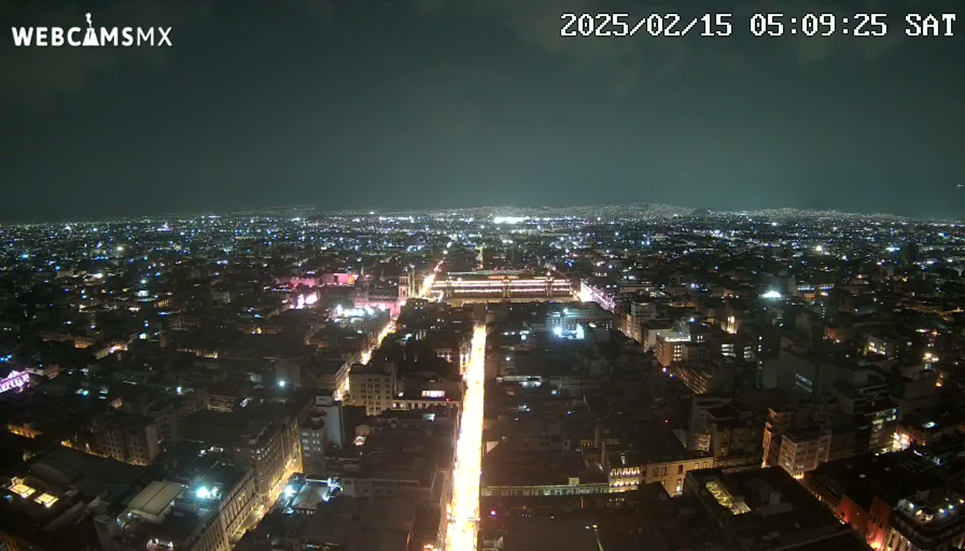 A nighttime aerial view shows a brightly lit city sprawling across a dark landscape under a clear sky.