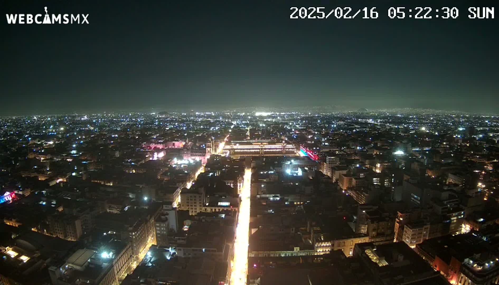 A nighttime aerial view shows a sprawling city with brightly lit streets and buildings under a clear, dark sky.