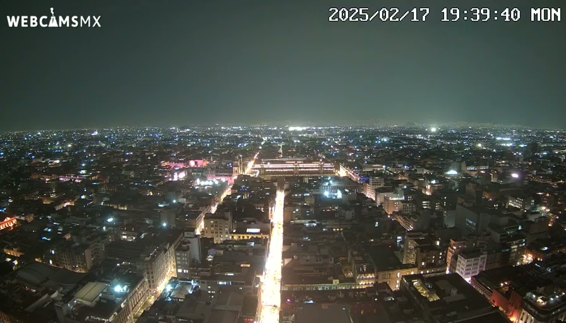 A nighttime aerial view shows a sprawling city with brightly lit streets and buildings under a clear, dark sky.