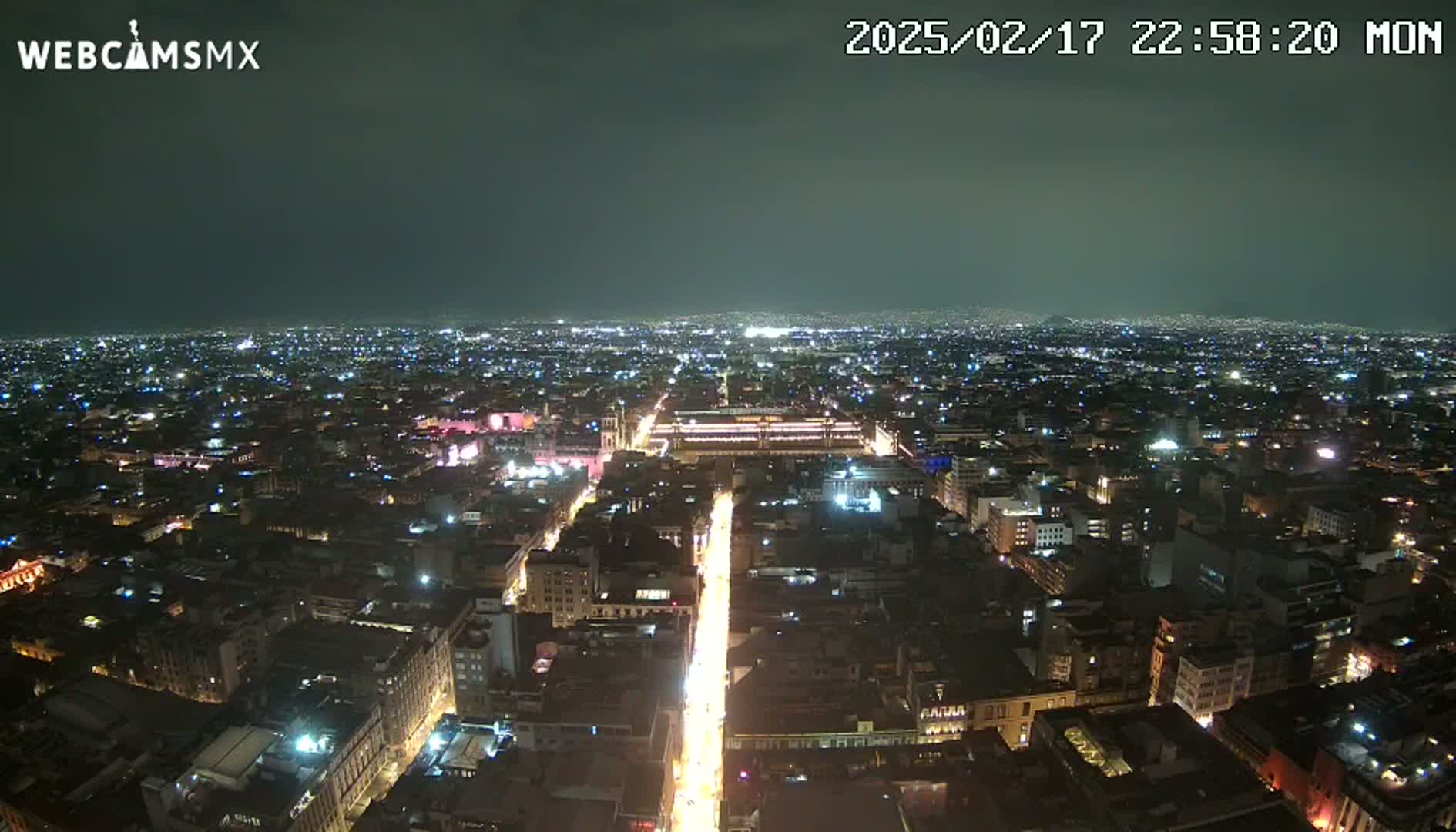 A nighttime aerial view of a sprawling city with brightly lit streets and buildings under a clear, dark sky.