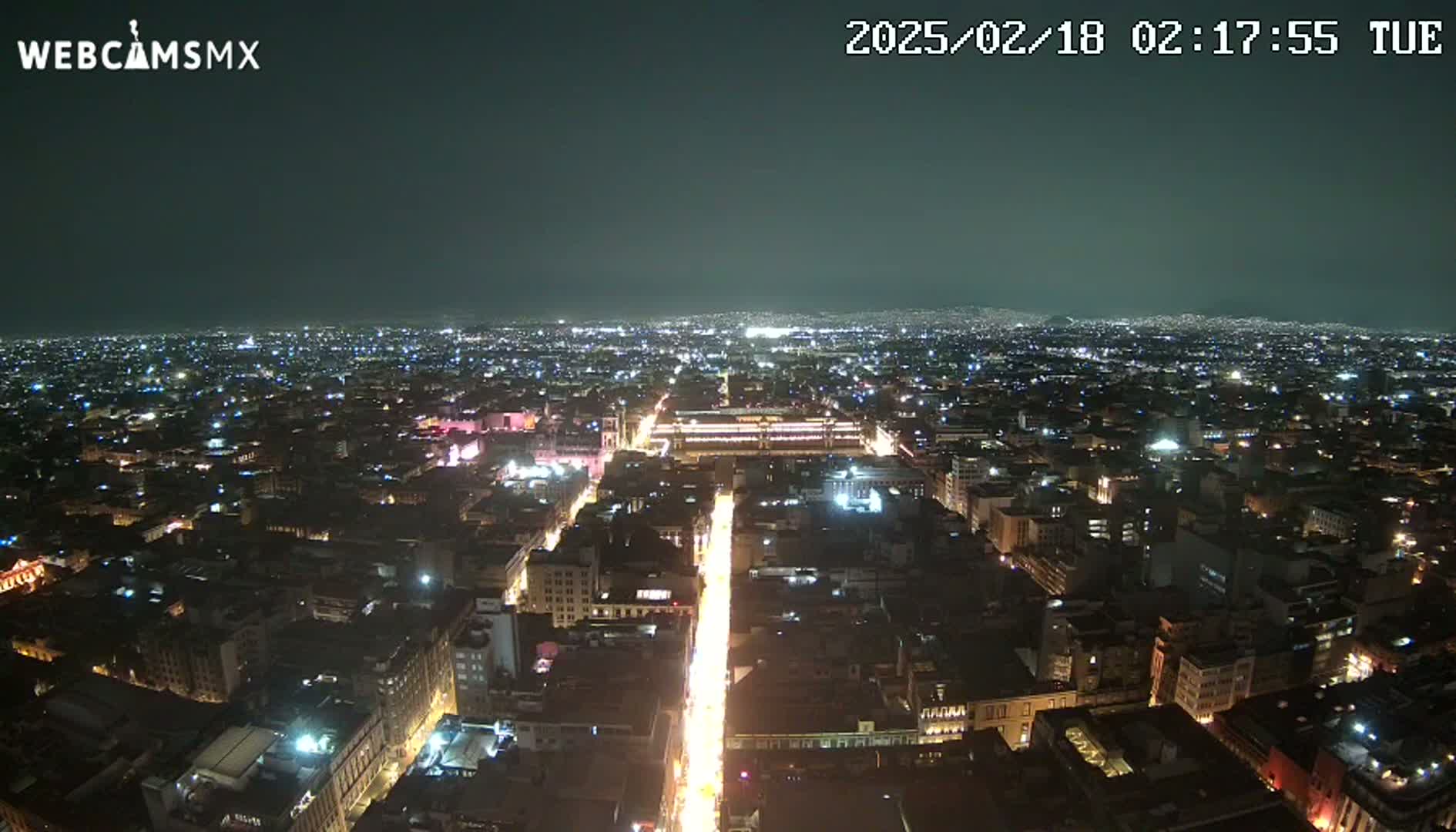 A nighttime, aerial view of a brightly lit city, extending to a dark horizon under a clear sky.