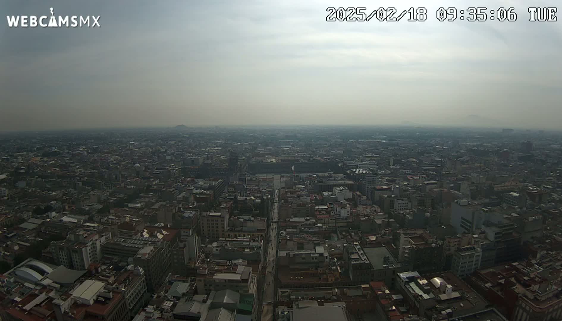A hazy, overcast view of a sprawling city from a high vantage point, showing a dense network of buildings and streets stretching to the horizon.