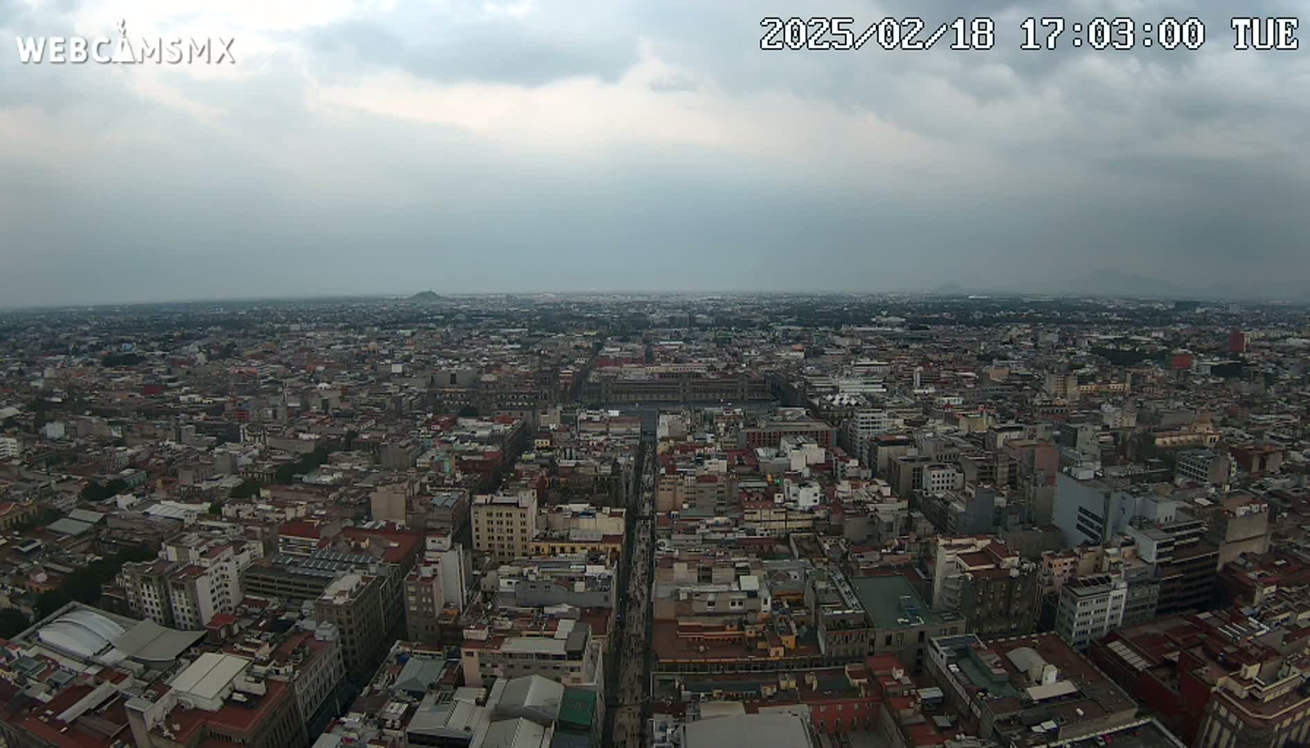 An aerial view of a vast city under an overcast sky shows densely packed buildings extending to the horizon.