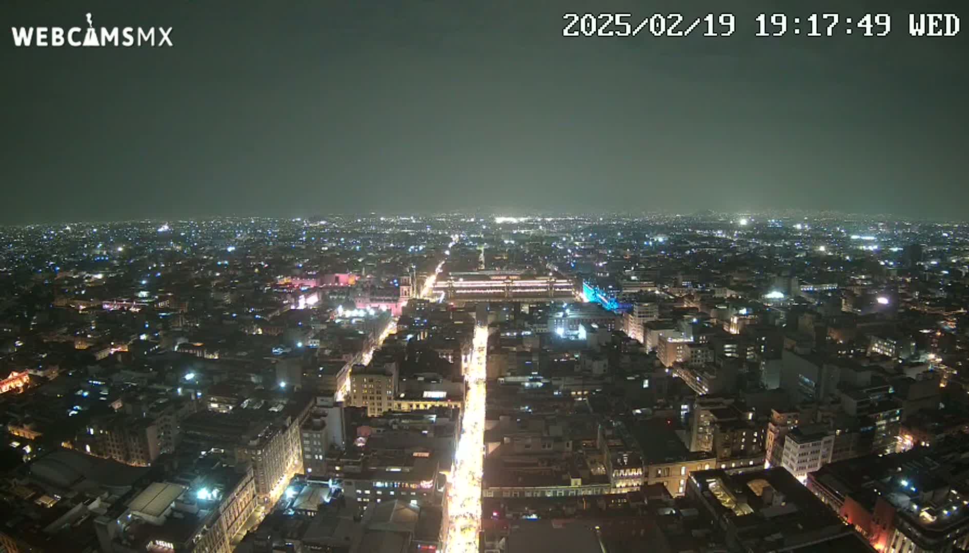 A nighttime aerial view of a sprawling city with brightly lit streets and buildings under a clear, dark sky.