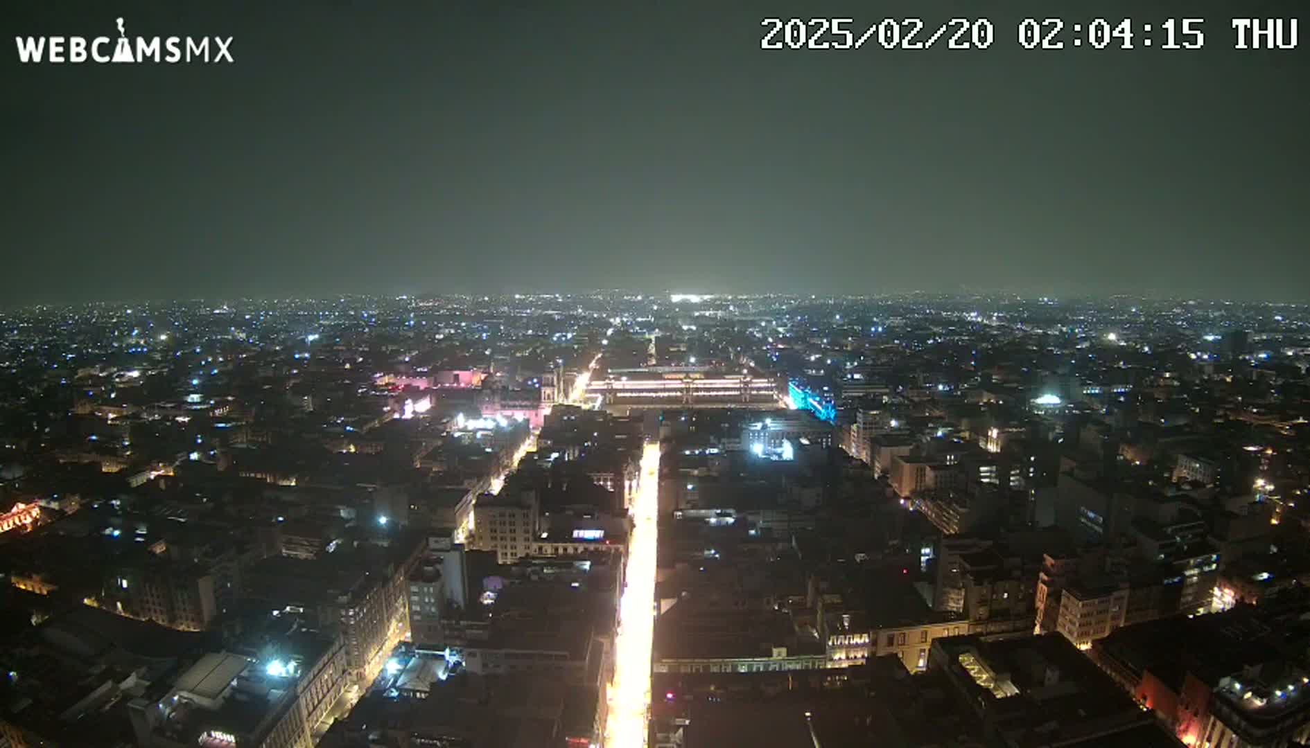 A nighttime aerial view of a city with a brightly lit street extending from the foreground to the distant horizon under a clear, dark sky.