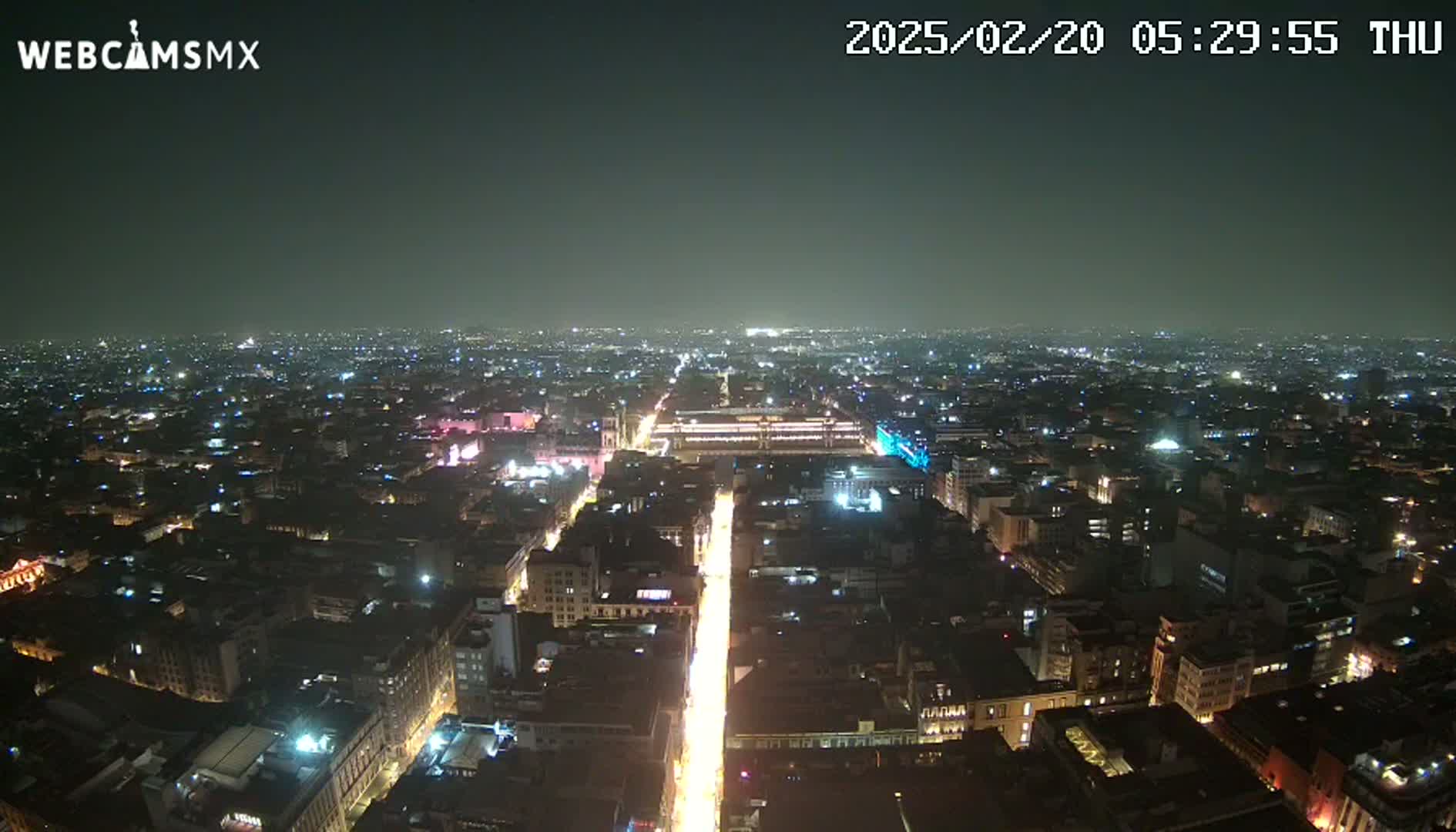 A nighttime, high-angle view of a city illuminated by streetlights and building lights under a dark, clear sky.