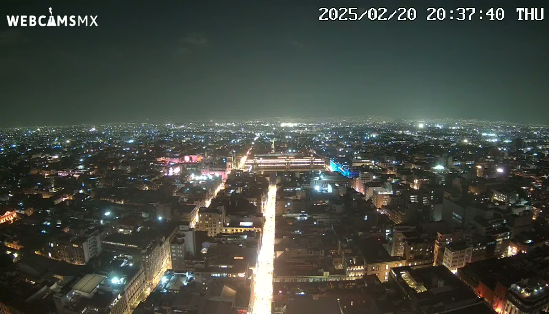 A nighttime aerial view shows a sprawling city with brightly lit streets and buildings under a clear, dark sky.