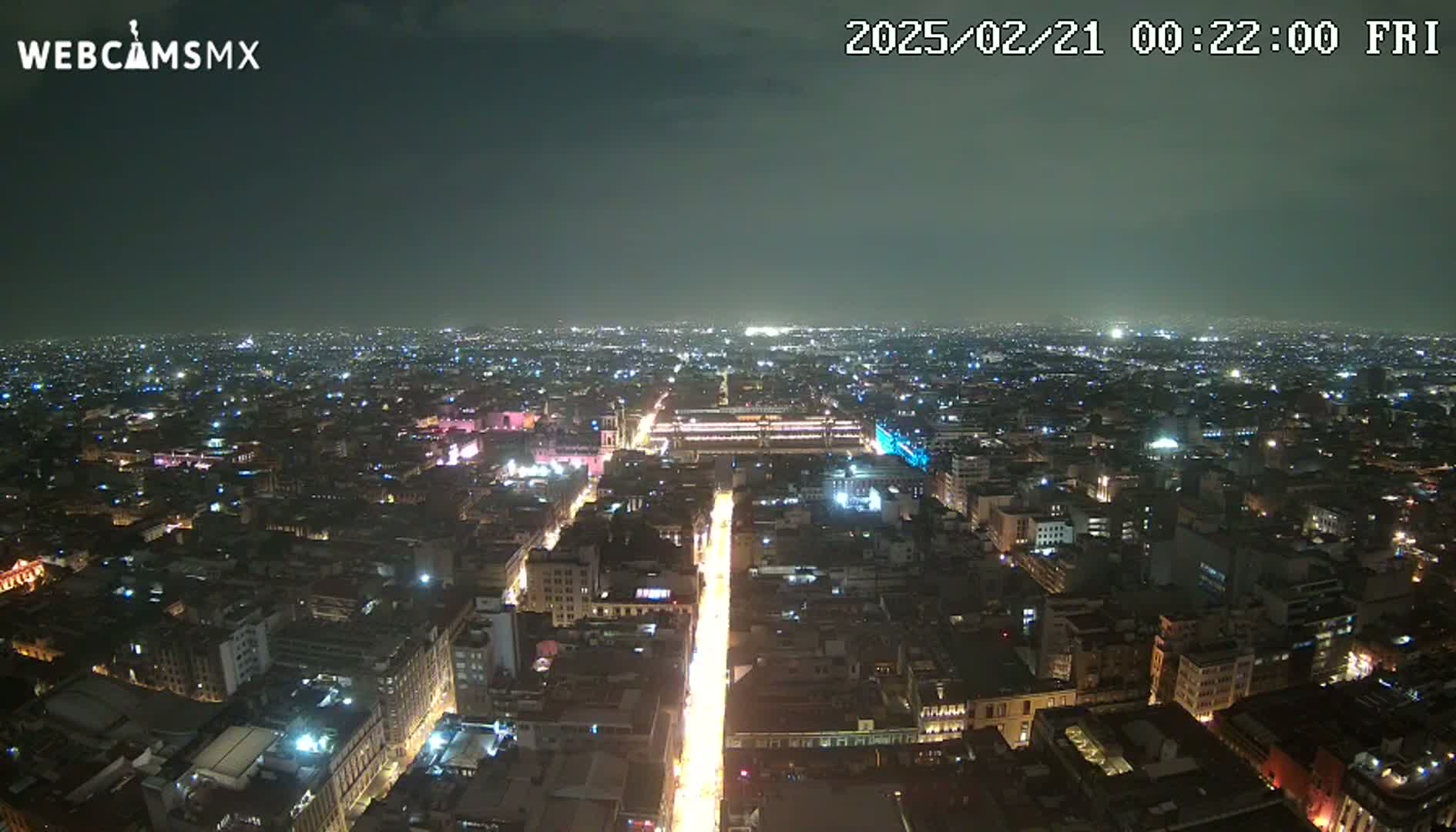 A nighttime, high-angle view shows a sprawling city with brightly lit streets and buildings under a mostly clear sky.