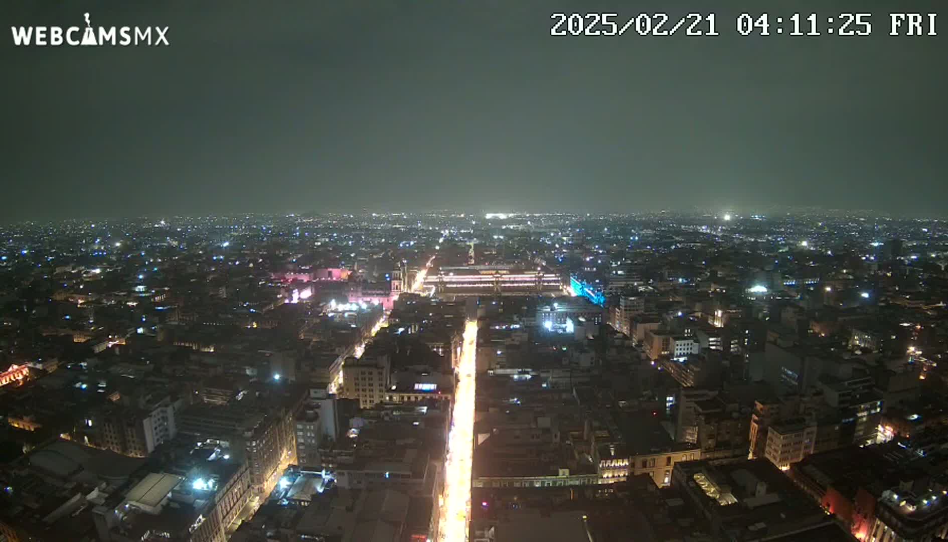 A nighttime aerial view of a city with a brightly lit street running through its center under hazy conditions.