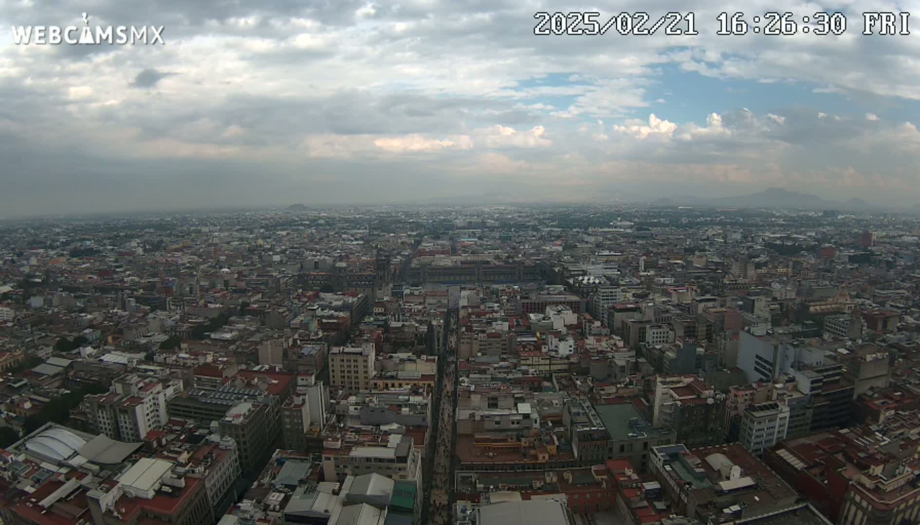 An aerial view of a sprawling city on a partly cloudy day shows many closely packed buildings extending to the horizon.