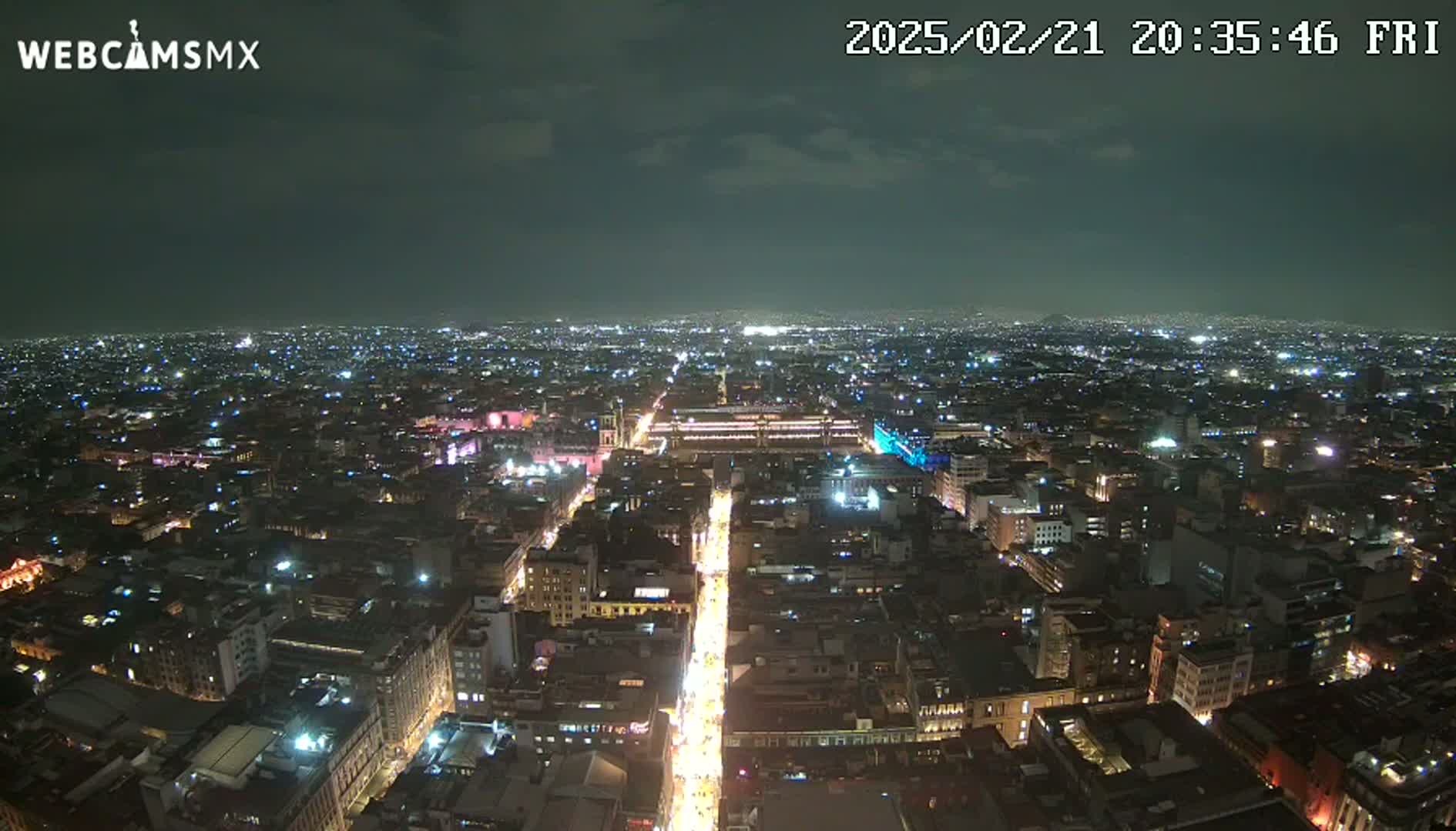 A nighttime aerial view of a brightly lit city under a partly cloudy sky.