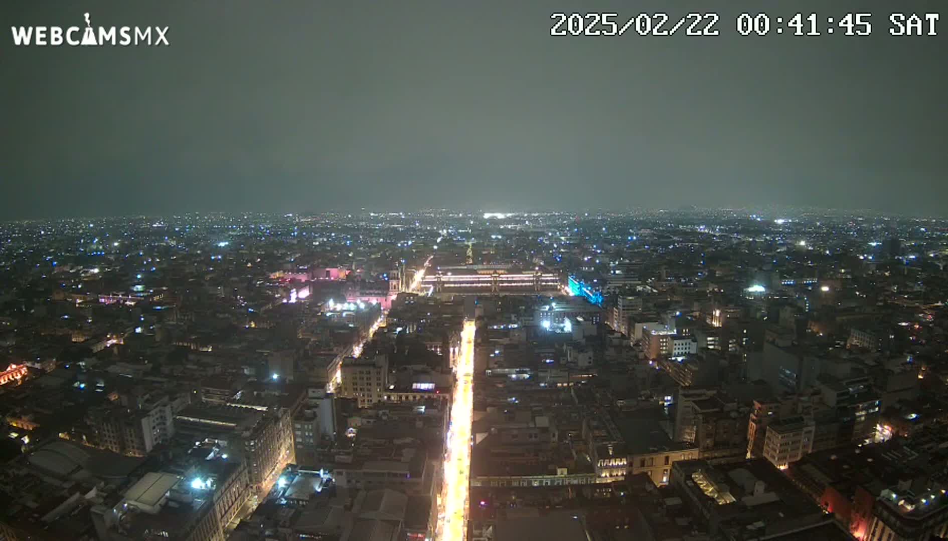 A nighttime, high-angle view of a sprawling city with dimly lit streets and buildings under a dark, overcast sky.