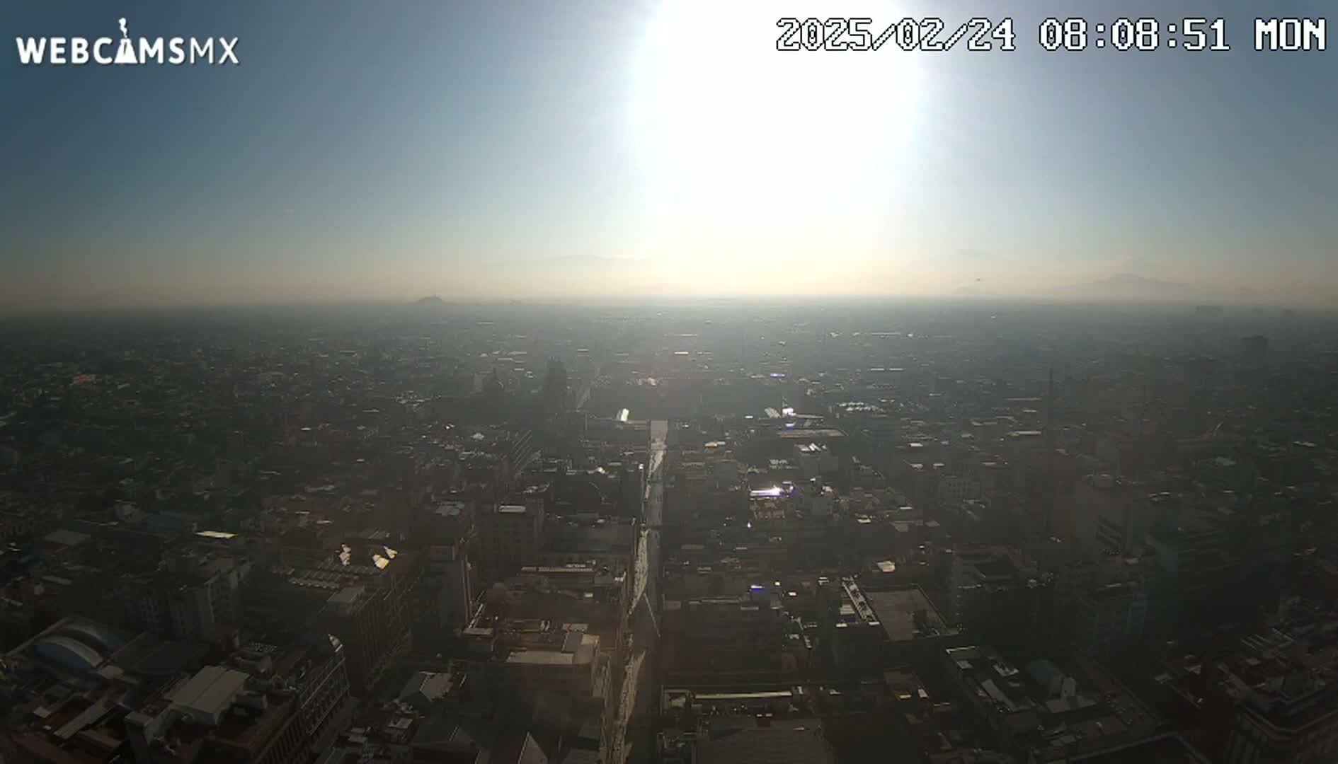 A hazy, sunny day reveals a sprawling cityscape viewed from a high vantage point.
