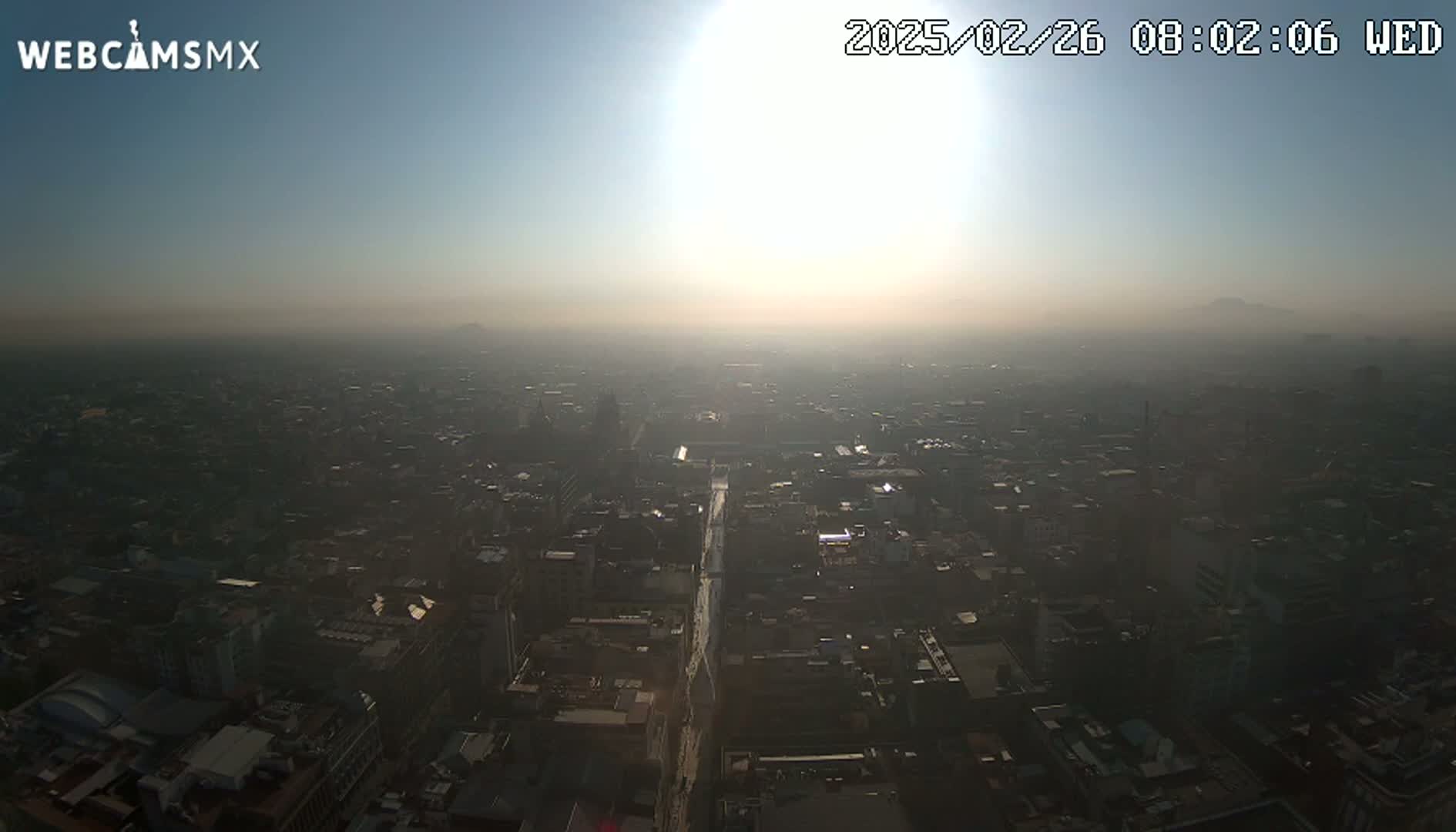 A hazy sunrise illuminates a sprawling cityscape, with a distant mountain barely visible through the atmospheric pollution.