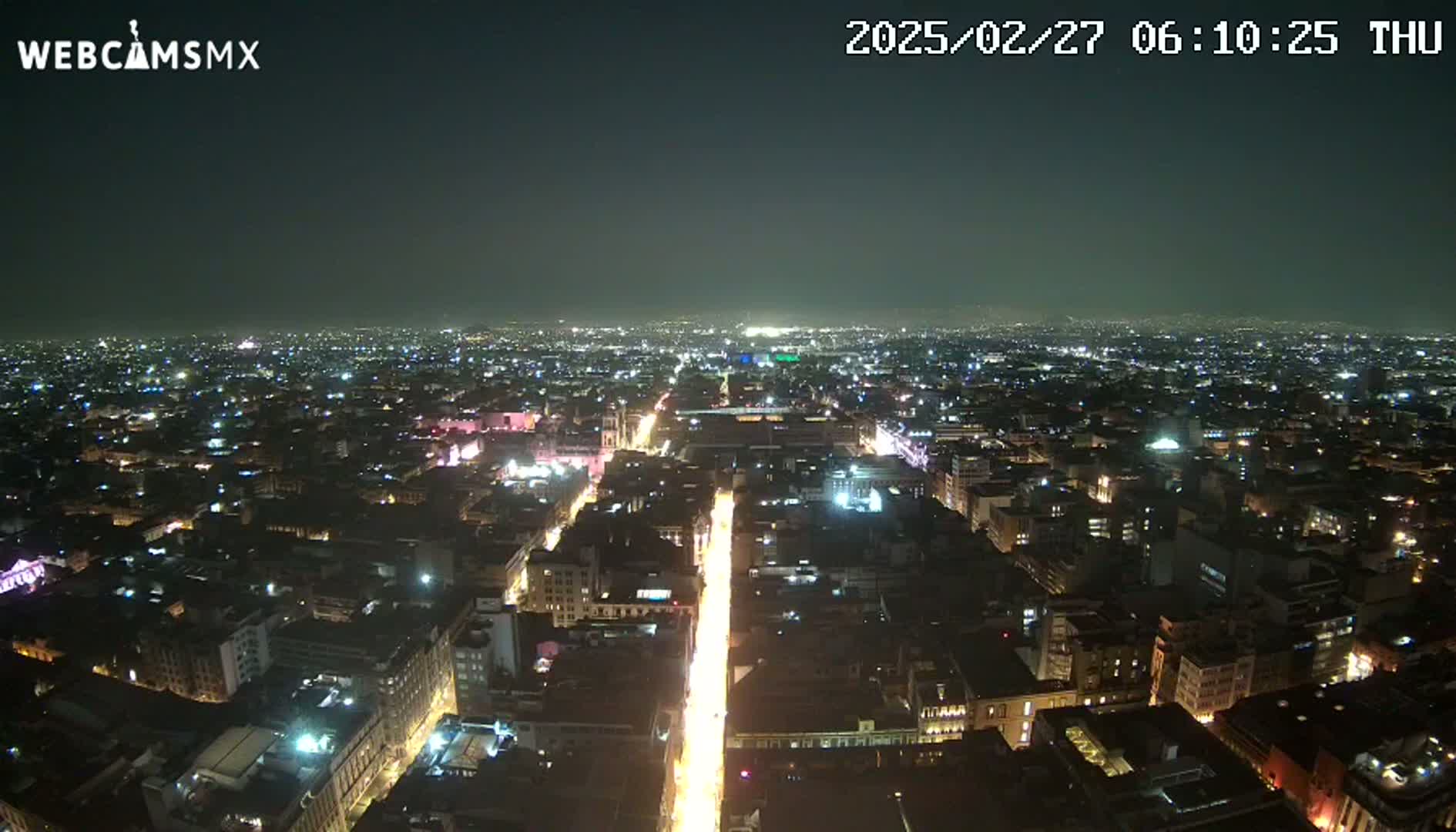 A nighttime, high-angle view of a sprawling city with brightly lit streets and buildings extending to the horizon under a clear, dark sky.