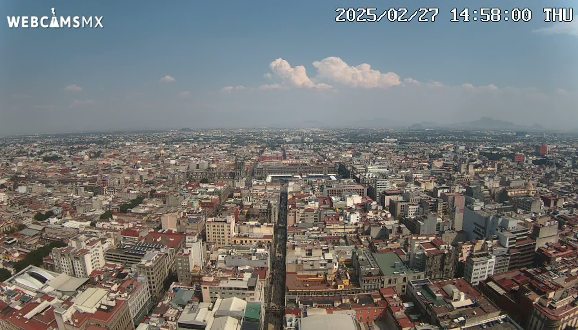 A high-angle, long shot of a sprawling city under a mostly clear sky with a few puffy clouds.