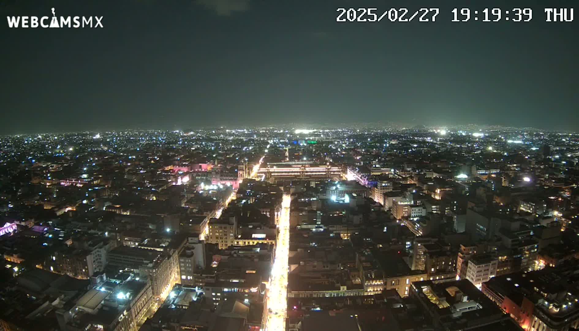 A nighttime, high-angle view of a sprawling city illuminated by countless lights.
