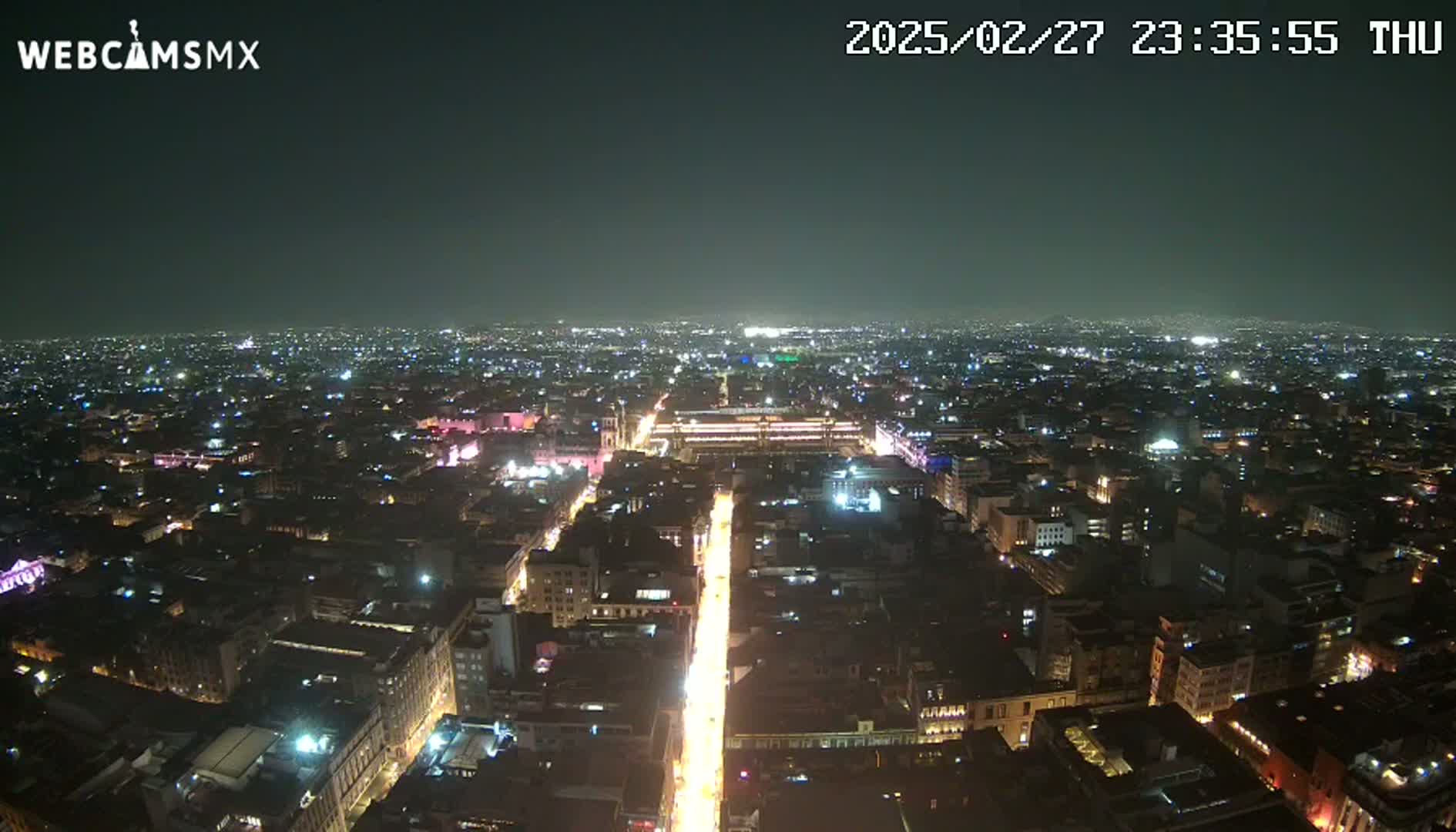 A nighttime aerial view of a city with a brightly lit street running through its center under a clear sky.