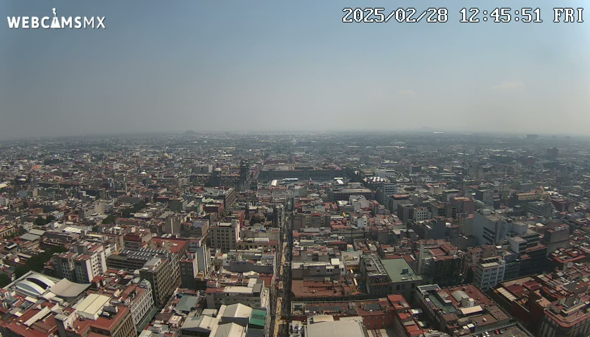 An expansive, hazy cityscape stretches to the horizon under a clear, bright sky.