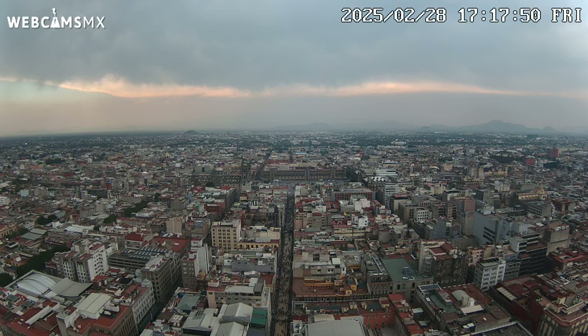 An expansive cityscape stretches under an overcast sky, with distant mountains visible on the horizon.