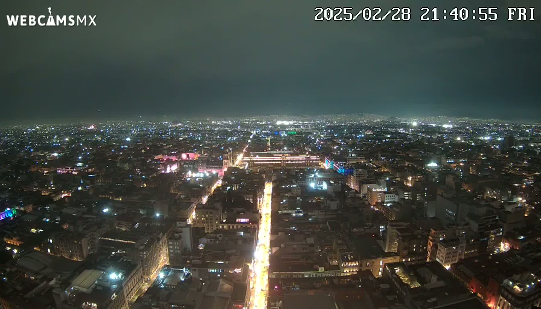 A nighttime aerial view of a sprawling city with brightly lit streets and buildings under a dark, clear sky.