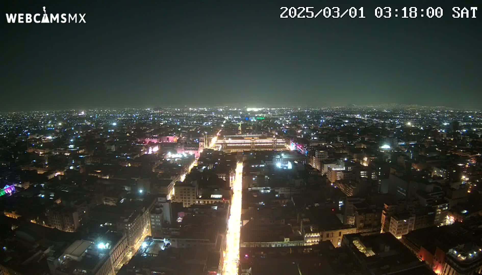 A nighttime aerial view of a city with brightly lit streets and buildings under a clear, dark sky.
