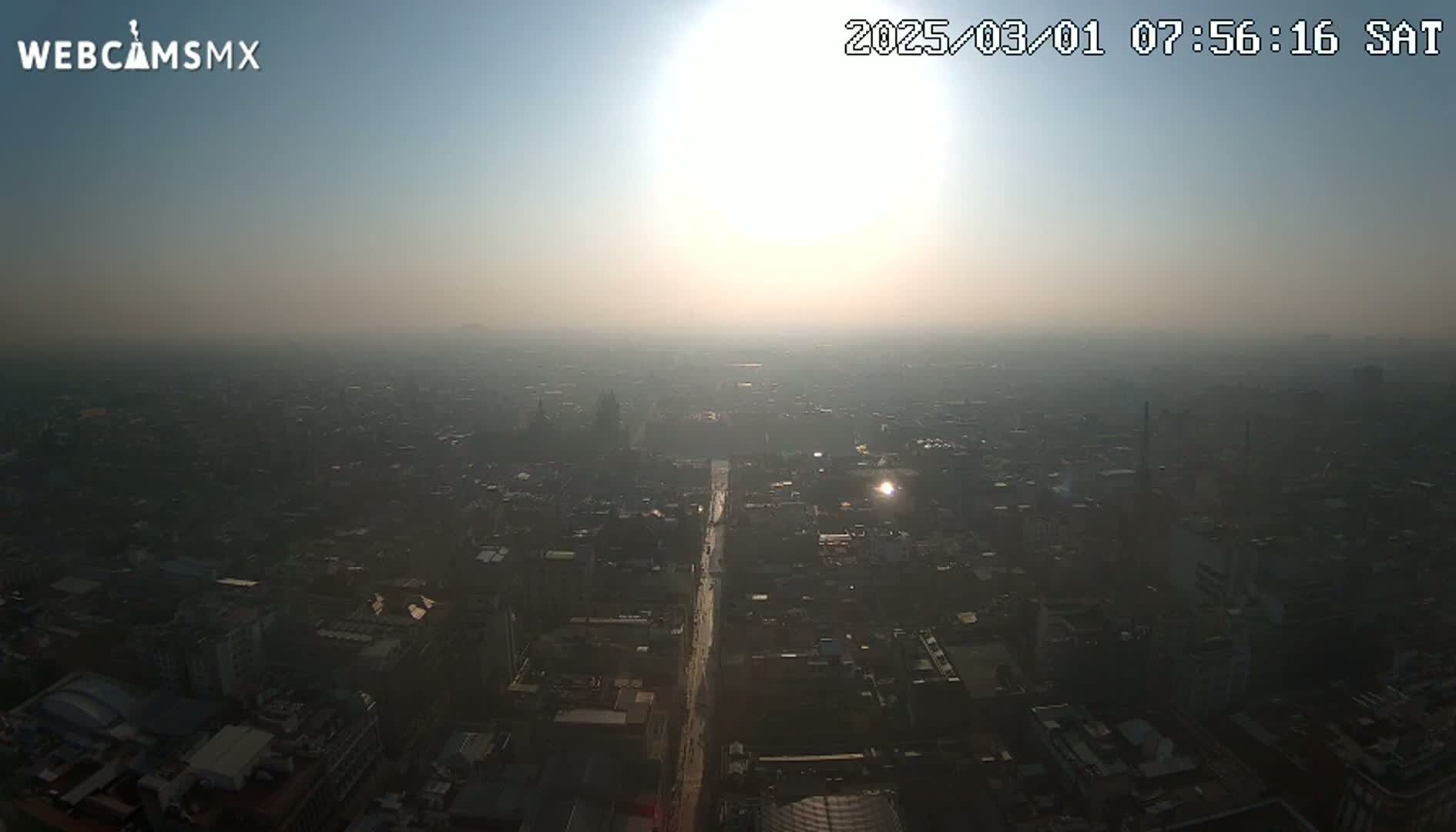 A hazy sunrise illuminates a sprawling city from a high vantage point.