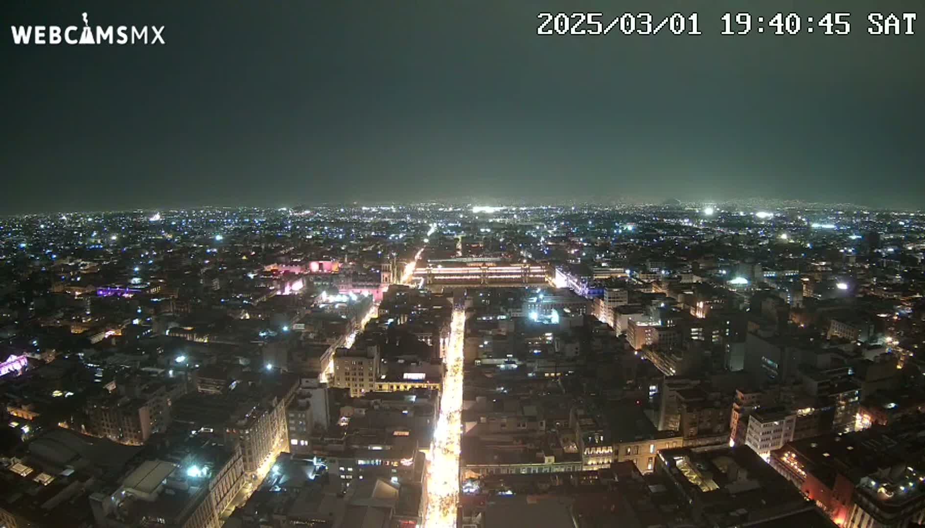 A nighttime aerial view of a brightly lit city sprawling across a dark landscape under a clear sky.